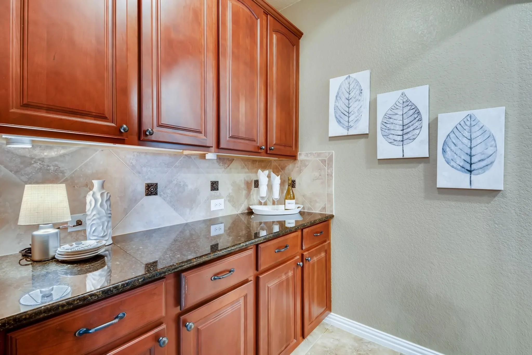 Rich wood cabinetry, stone countertops, tiled backsplash, under-cabinet lighting, and tiled flooring