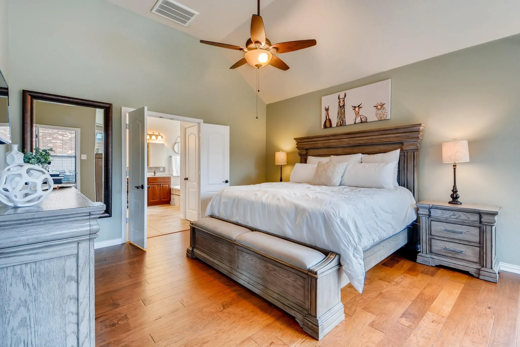 Vaulted ceiling with a ceiling fan, wood-finish flooring, and double doors to a bathroom
