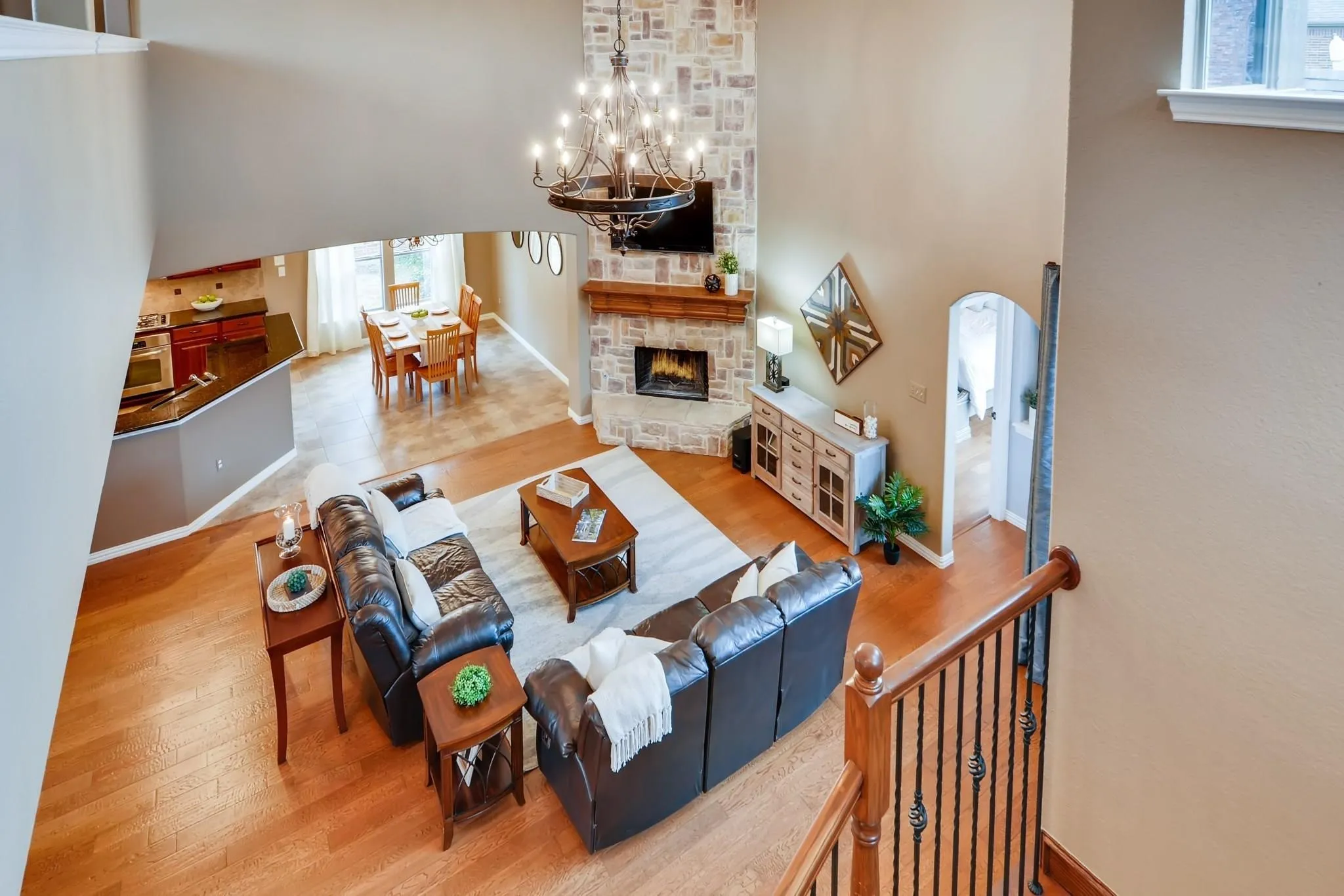 Two-story living area with hardwood flooring, a stone-faced fireplace, and an ornate chandelier