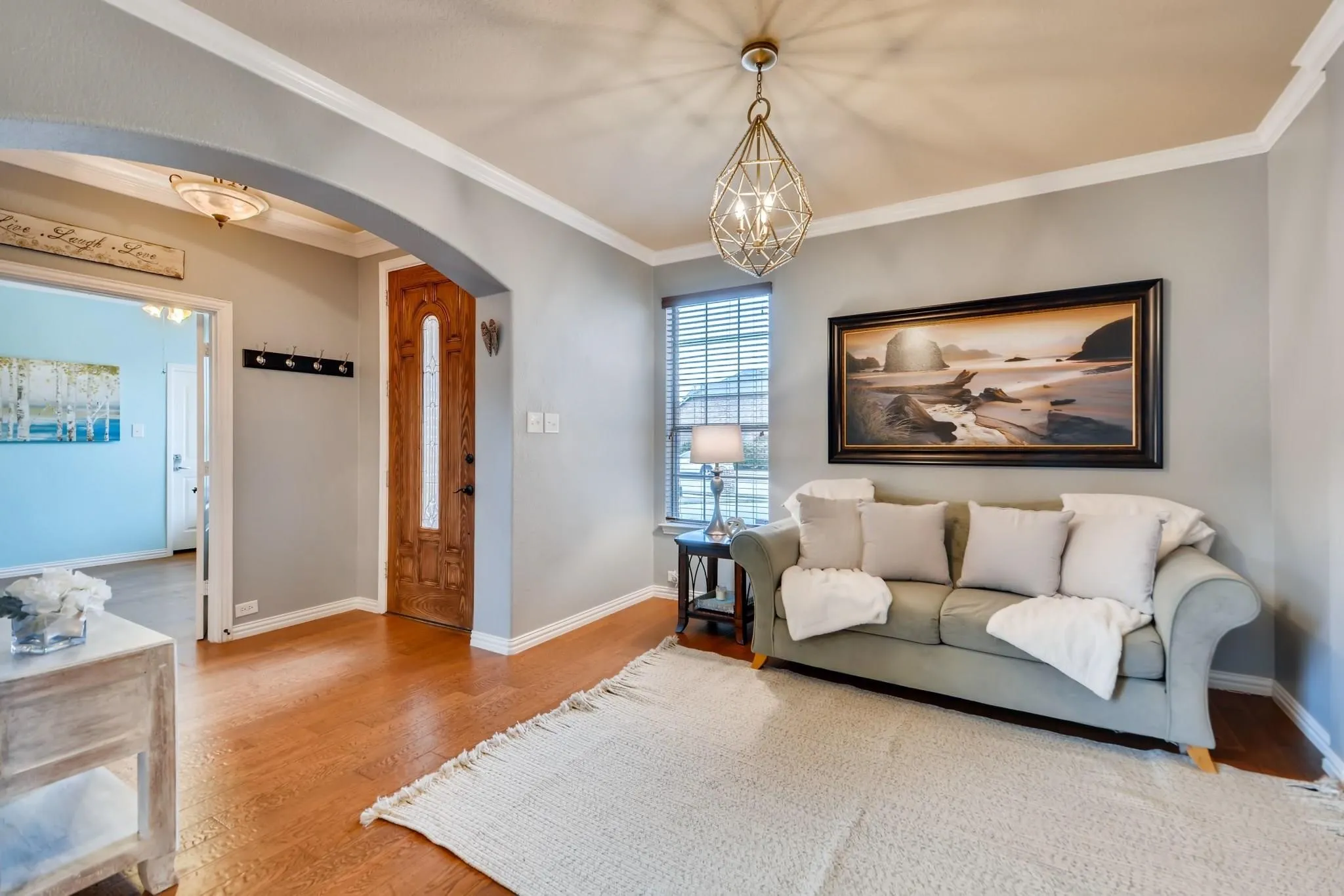 Wood-finish flooring, arched entryway, decorative ceiling light fixture, window with blinds, and crown molding