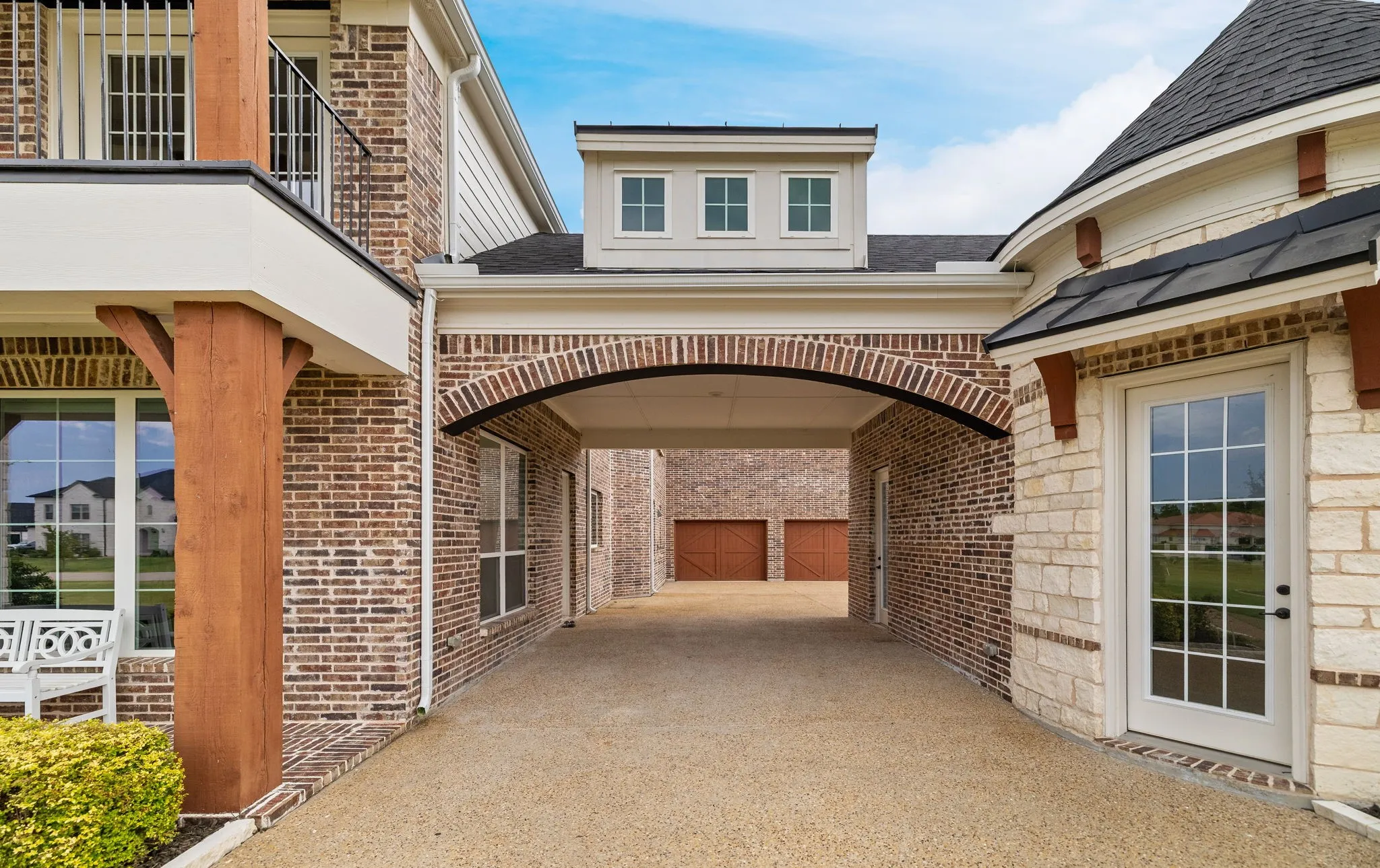 Brick and stone exterior with a porte-cochere, dormer windows, a balcony with iron railings, and a turretted entryway
