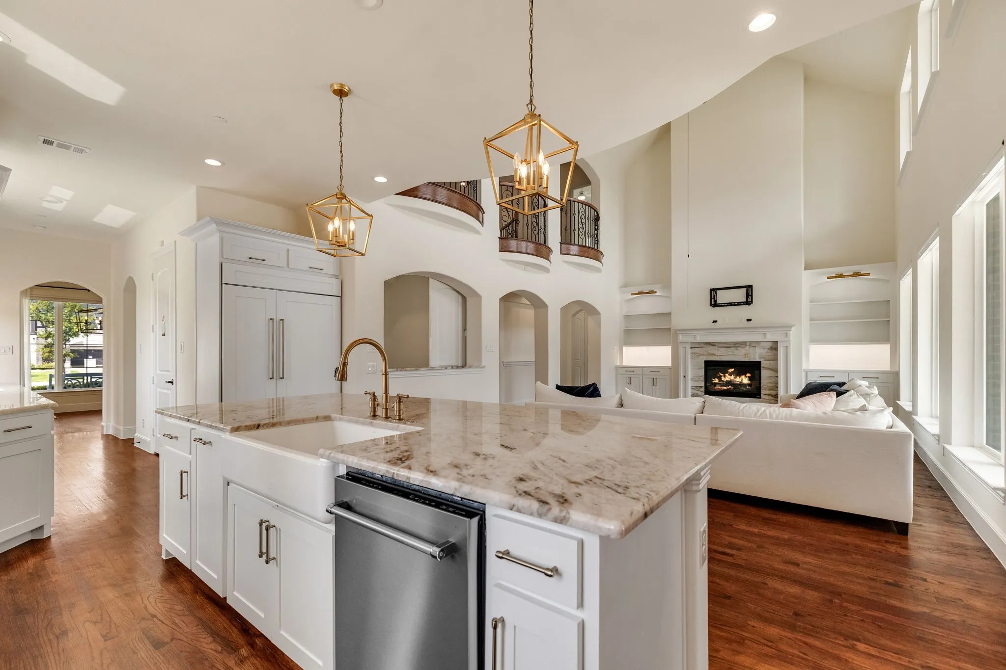 Gourmet kitchen with white cabinetry, a farmhouse sink, and stone countertops, complemented by wood-finish flooring