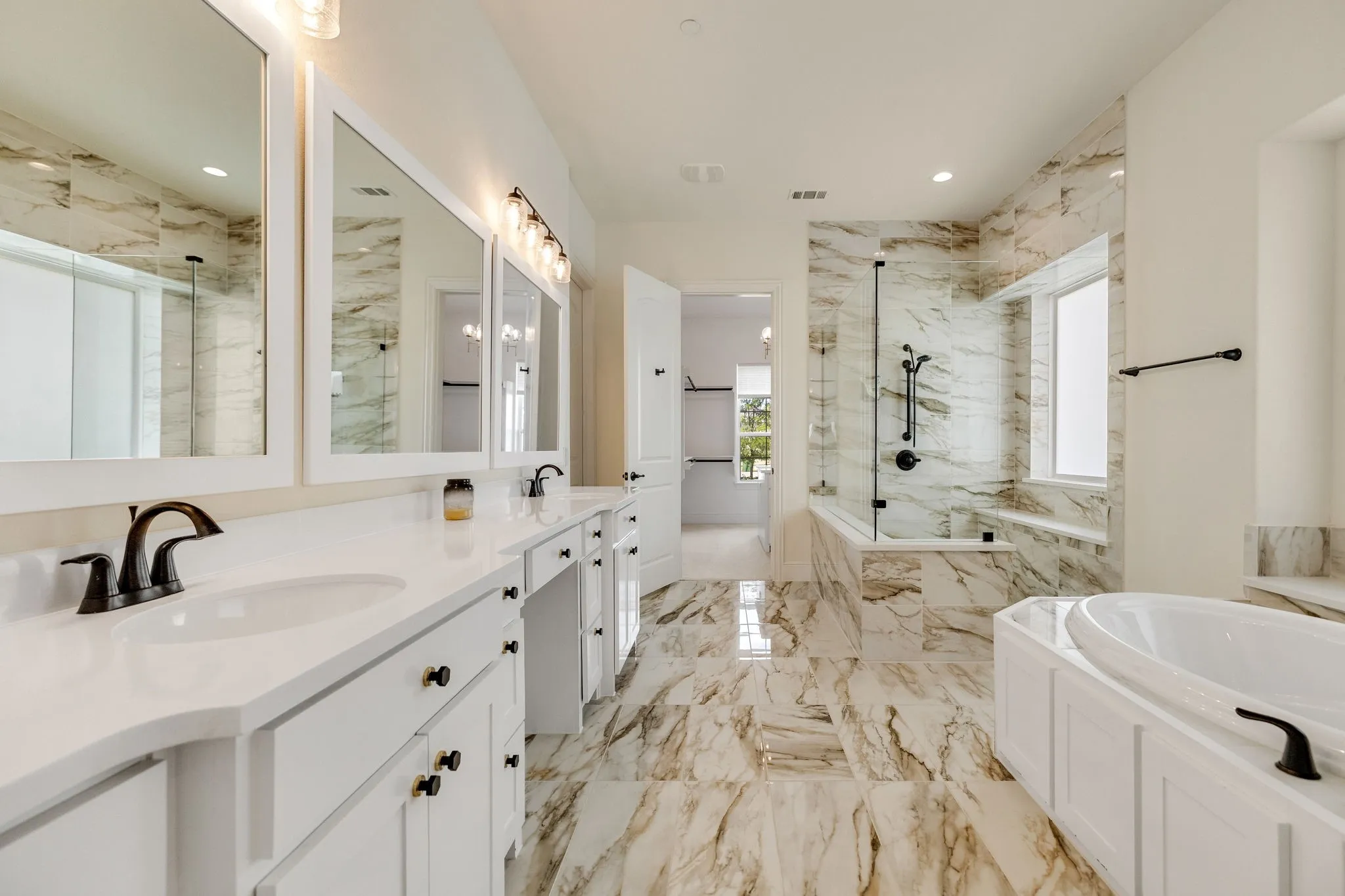 Dual vanities with white countertops, white cabinetry, a freestanding soaking tub, a walk-in shower with a glass enclosure, and large format marbled tile flooring