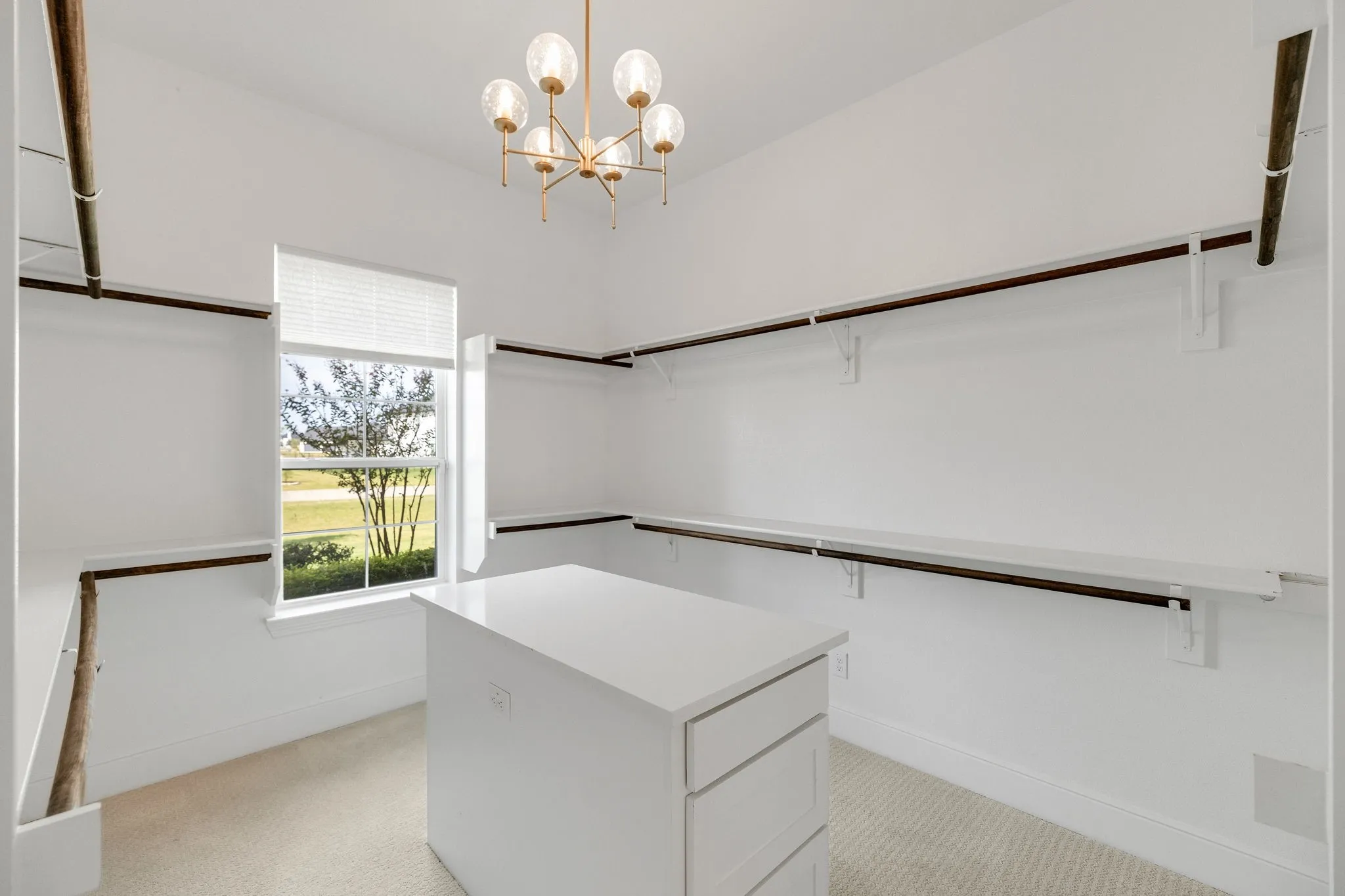 Built-in shelving and hanging rods, central island with drawers, single window, and a decorative chandelier