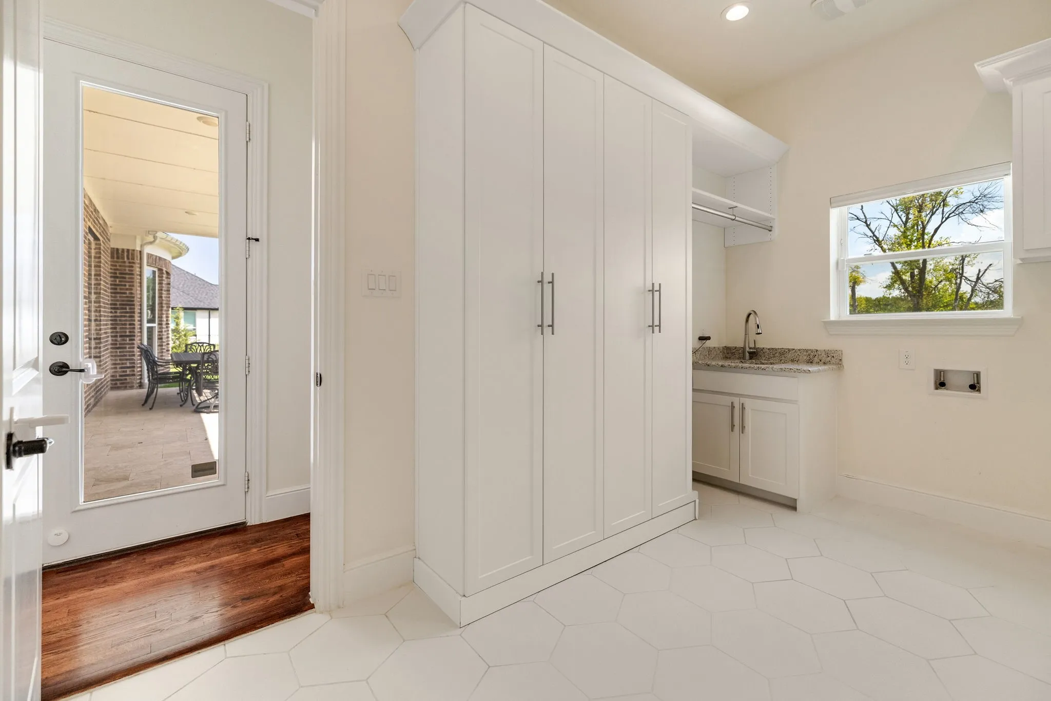 White hexagonal tile flooring, built-in white cabinetry, granite countertop with integrated sink, and direct access to an outdoor patio