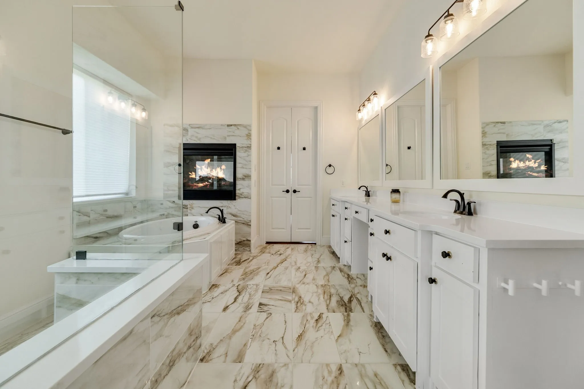 Freestanding soaking tub with a built-in fireplace, dual vanities with white cabinetry, framed mirrors, and a glass-enclosed shower