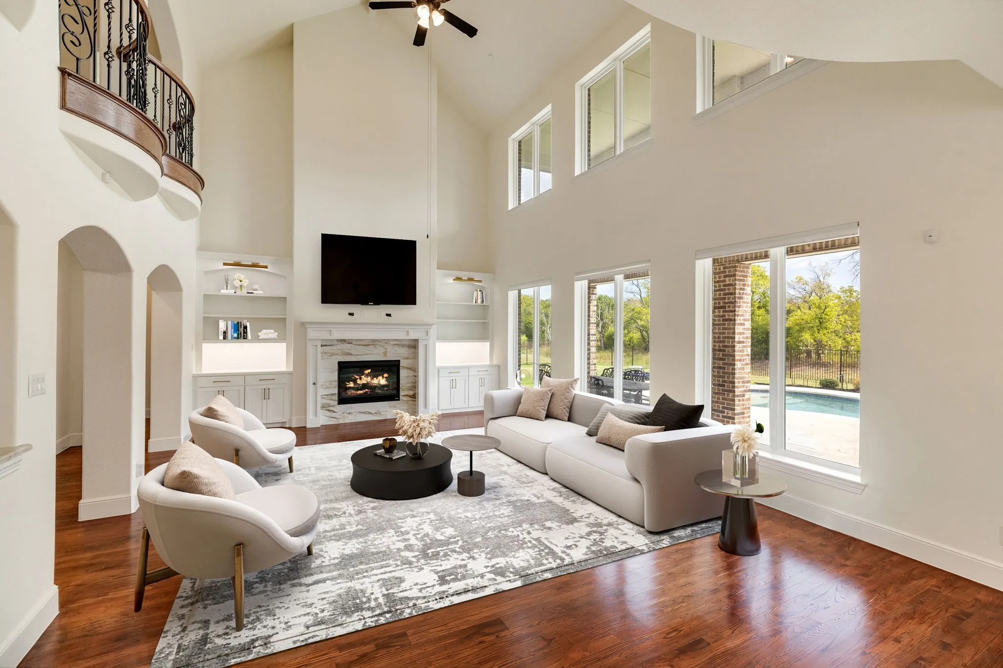 Living Room virtually staged, Two-story living area with wood-finish flooring, a fireplace featuring a stone surround, and built-in shelving with cabinetry
