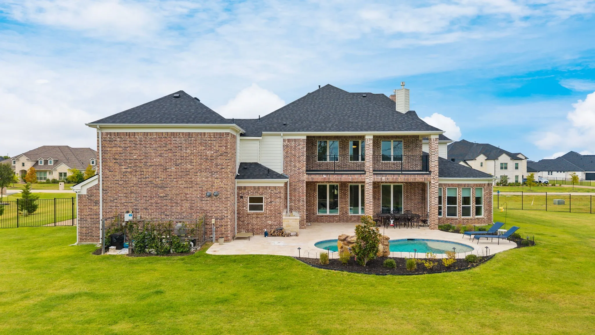 Brick exterior with a covered patio, an in-ground swimming pool with a rock water feature, and an expansive lawn