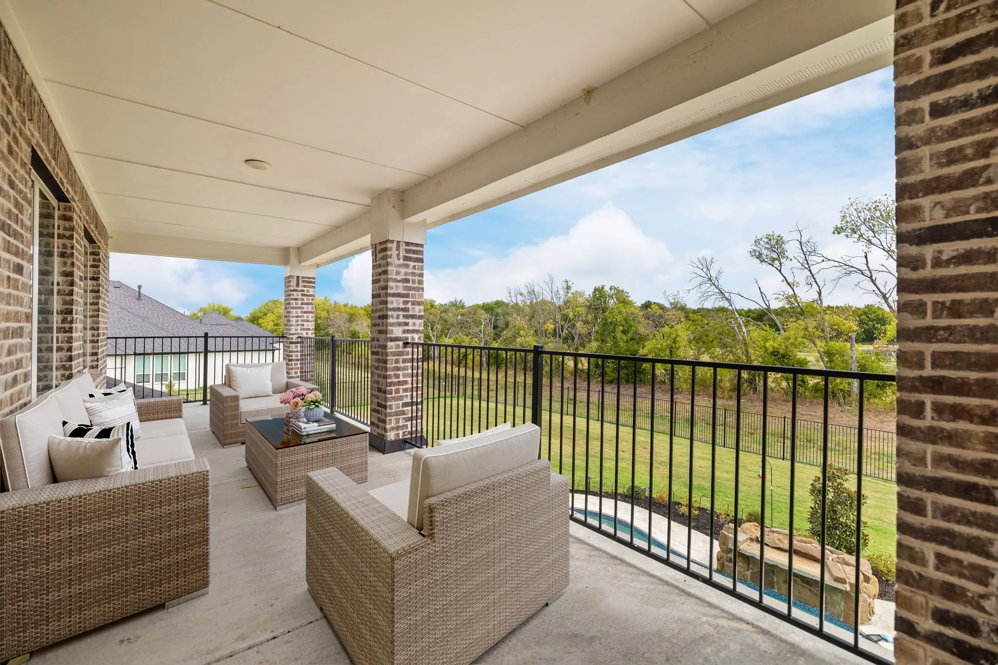 second level balcony virtually staged, Expansive covered patio featuring a concrete surface, brick columns, and a black metal railing