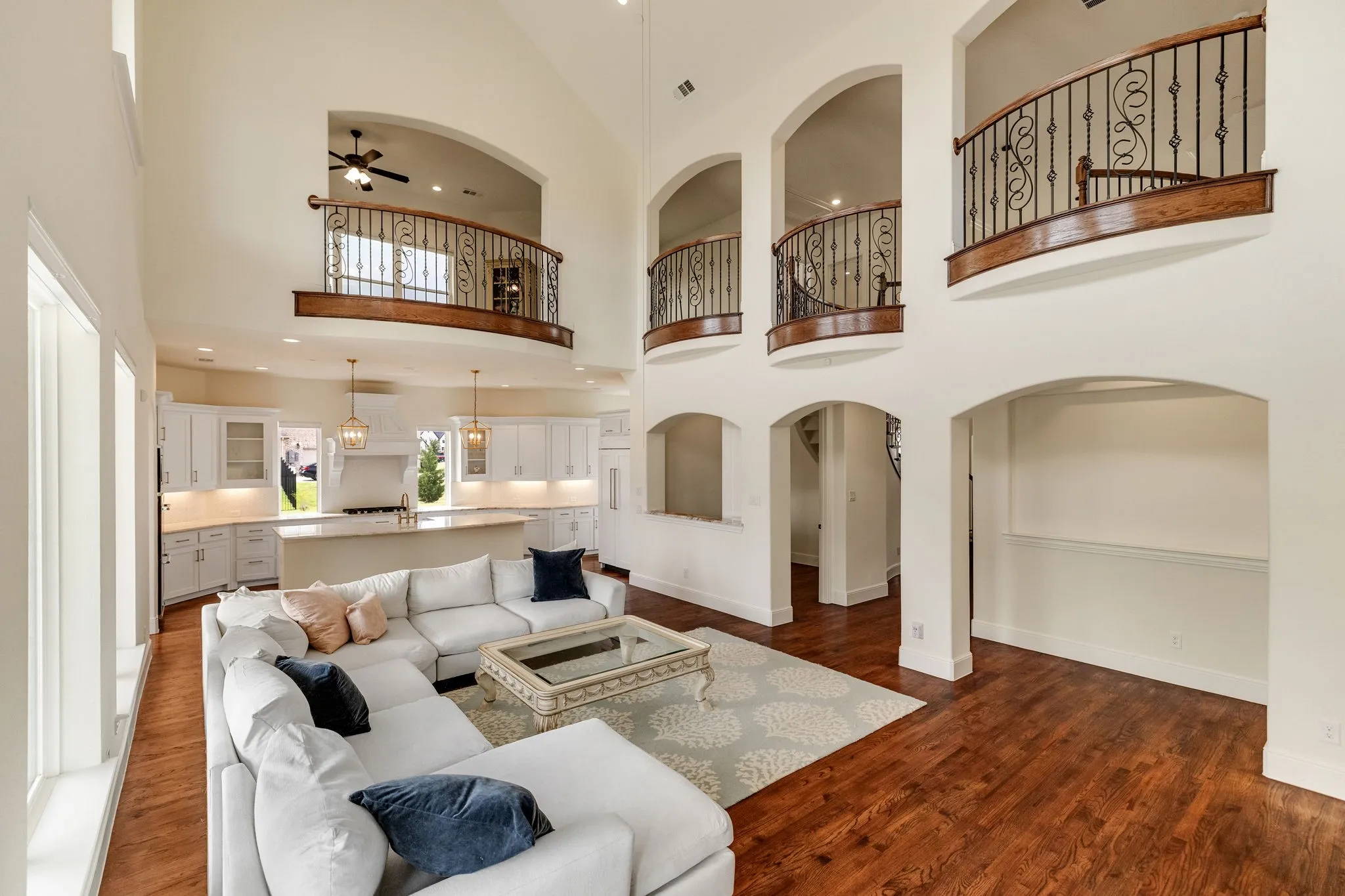 Vaulted ceilings, open concept kitchen, wood-finish flooring, wrought iron balustrades, and arched architectural details