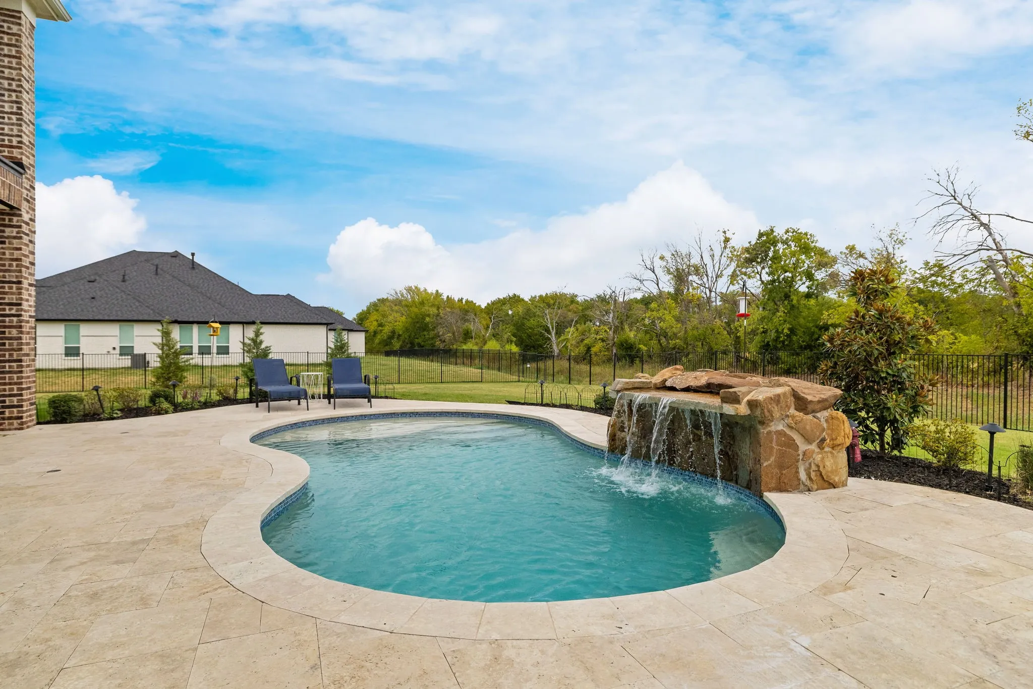 Freeform swimming pool with a rock waterfall feature, complemented by a paver patio and surrounding landscaping