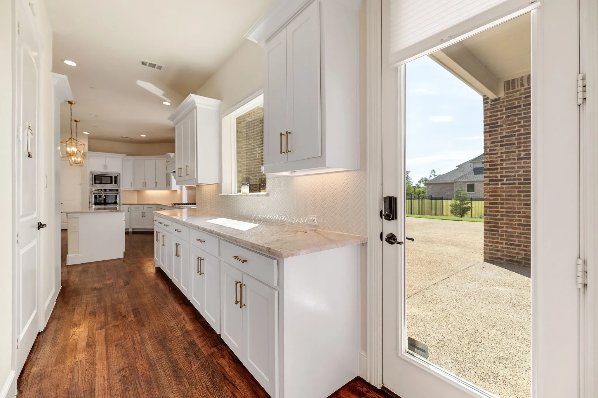 Wood-finish flooring, white cabinetry, integrated double ovens, recessed lighting, and a full-light exterior door