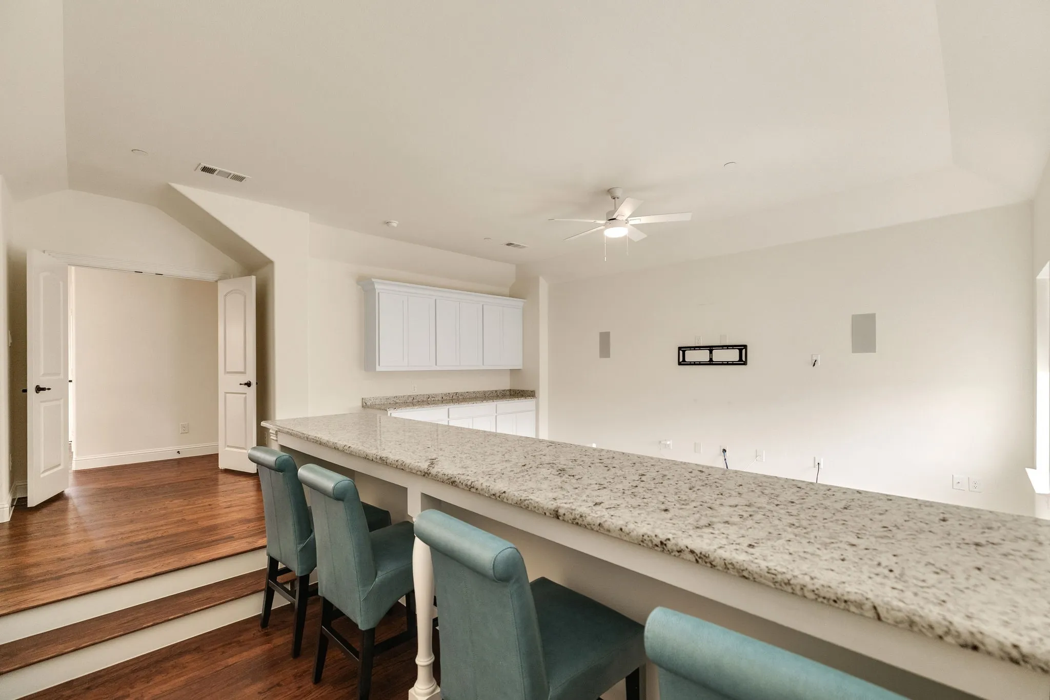 Raised platform with wood-finish flooring, half-wall with a granite countertop, white cabinetry with built-in countertop, and ceiling fan