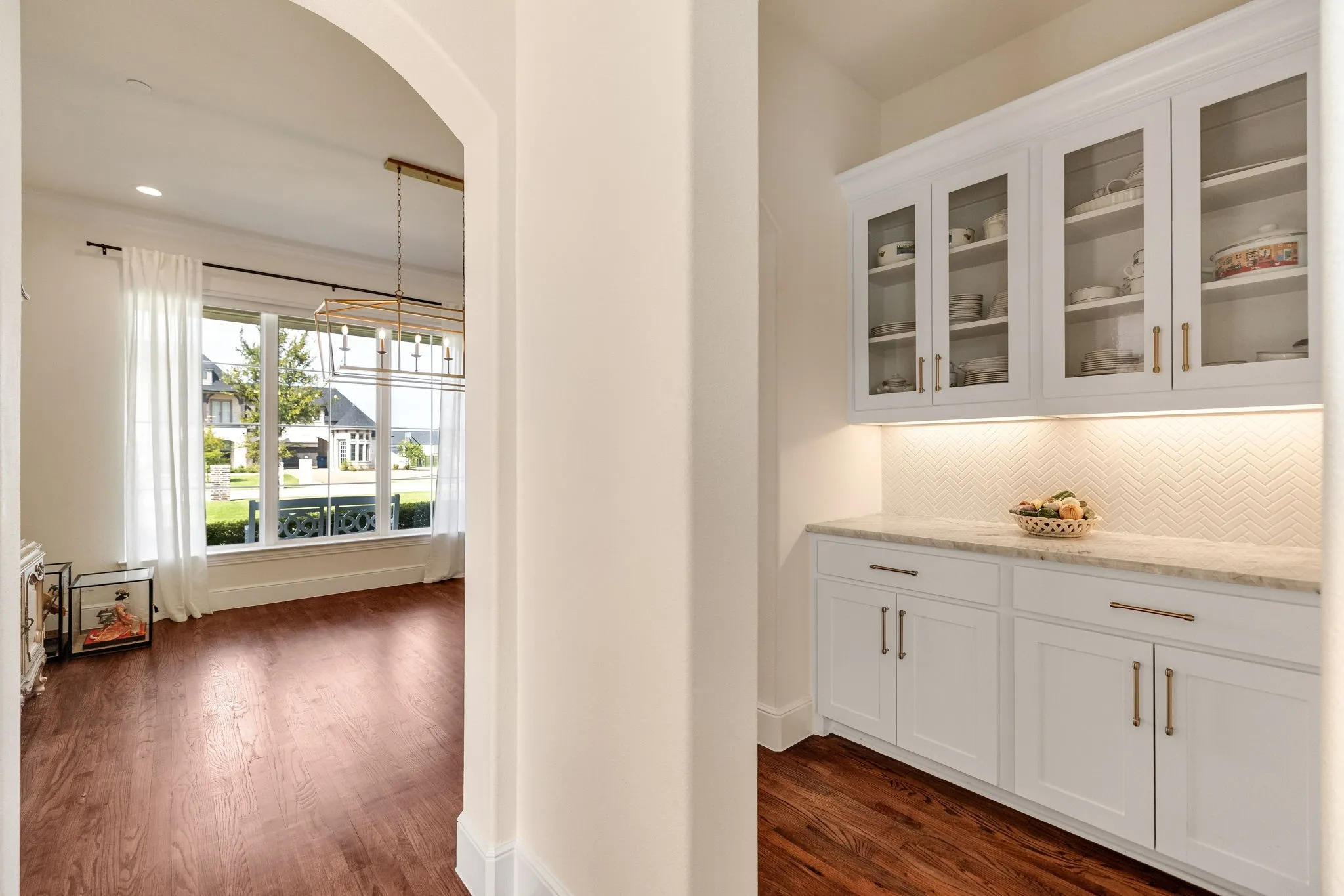 Built-in cabinetry with glass-front uppers, a light-toned countertop, and a white herringbone tile backsplash