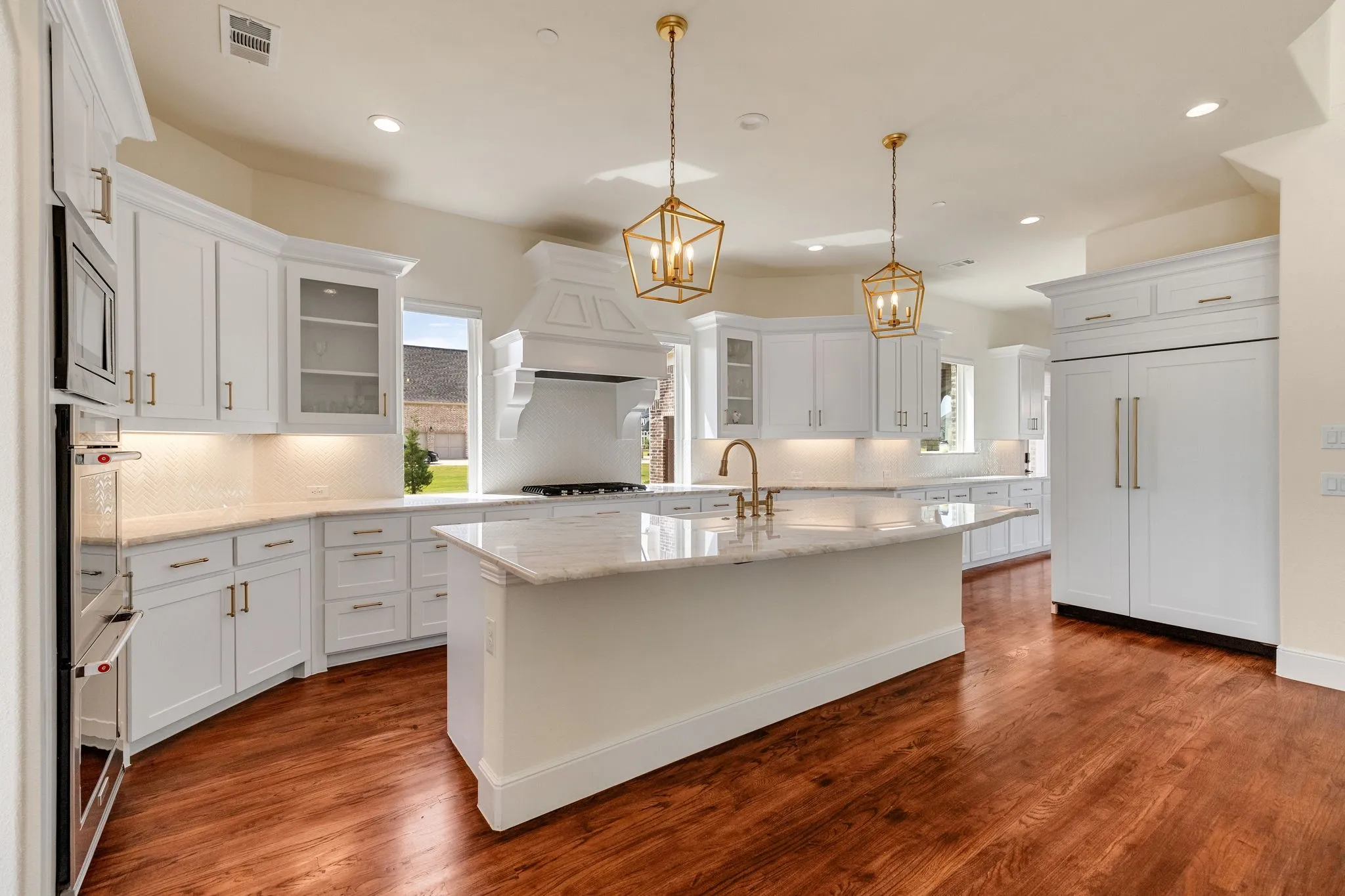 Gourmet kitchen with white cabinetry, light-toned countertops, a large island, wood-finish flooring, and built-in double ovens