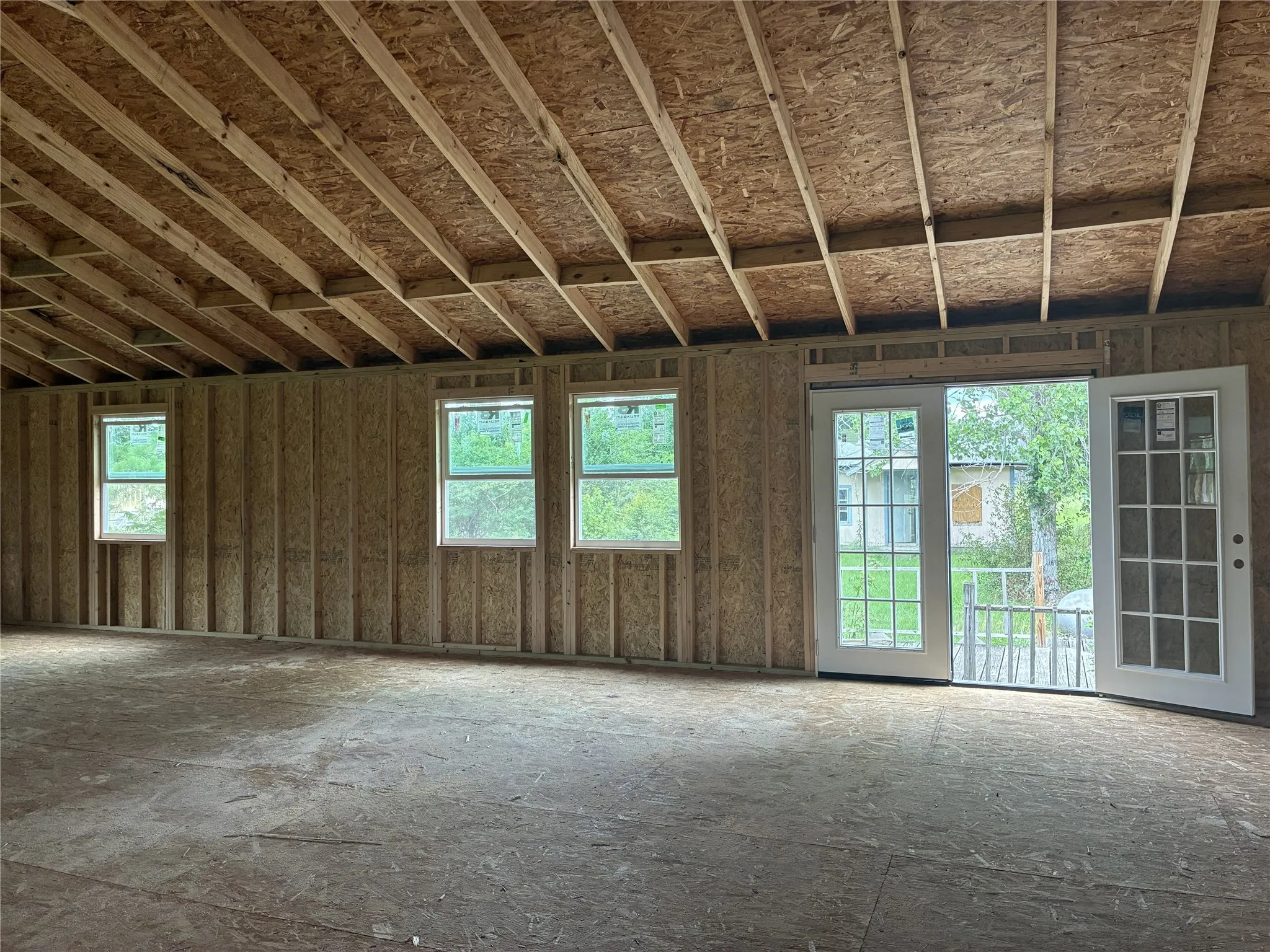Unfinished interior framing with exposed ceiling joists, multiple windows, and a double-door exterior entry