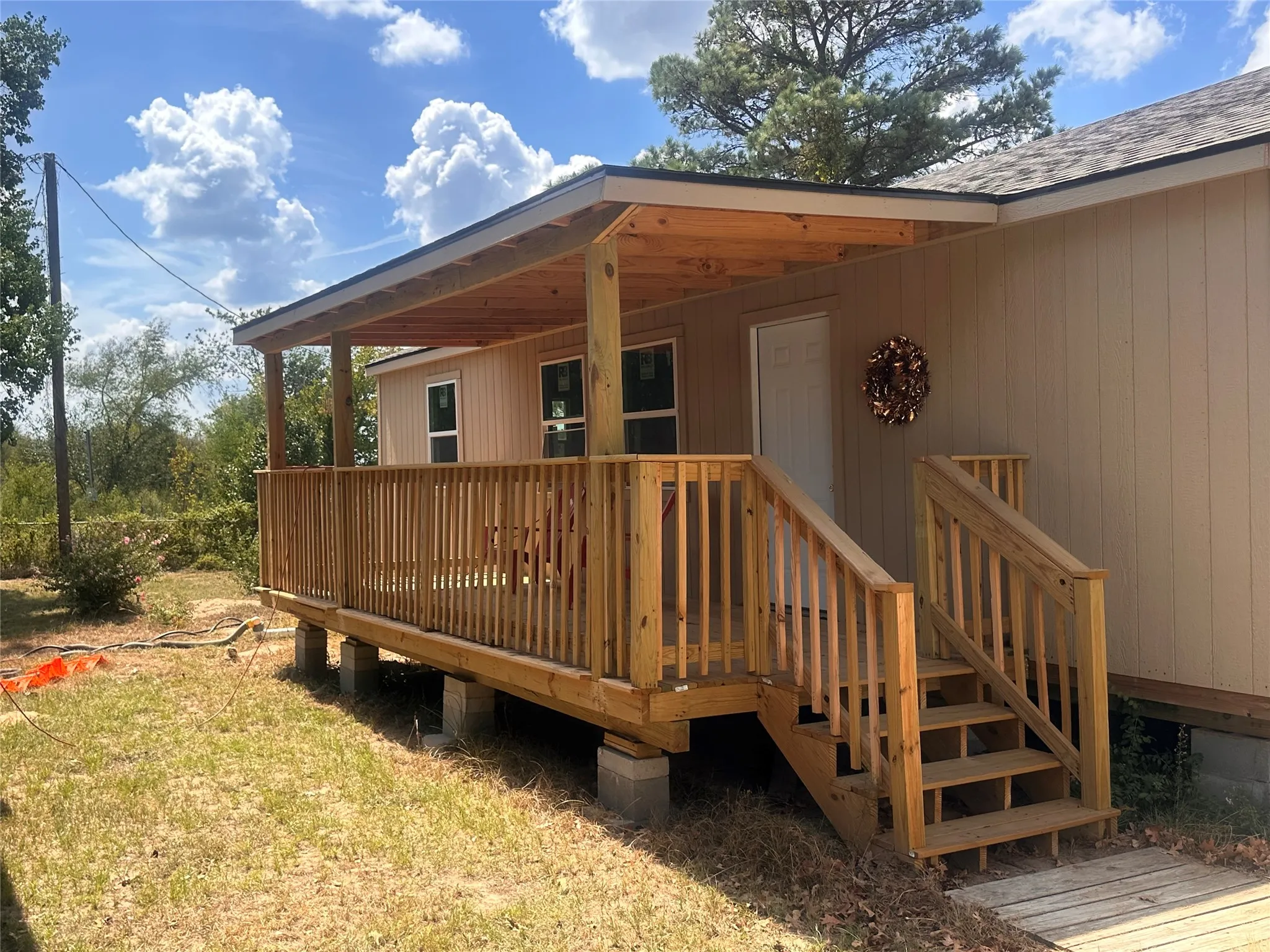 Covered front porch with wood-finish decking and railing, light-colored vertical siding, and a white entry door