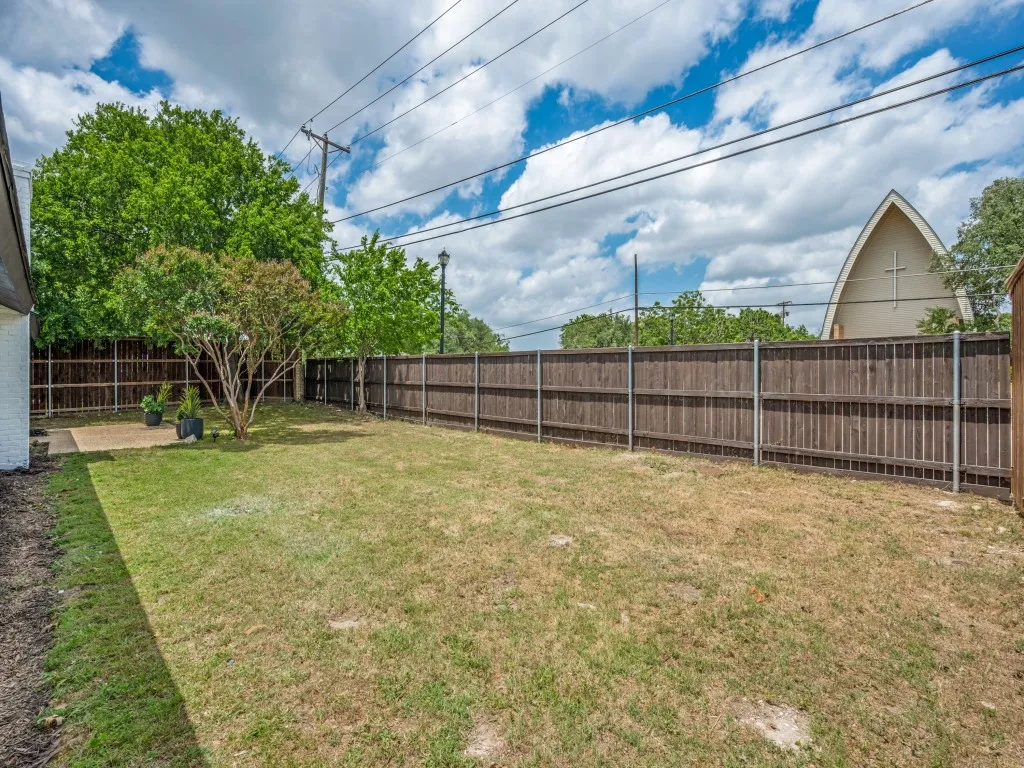 Expansive backyard featuring a wood privacy fence, mature trees, and a concrete patio