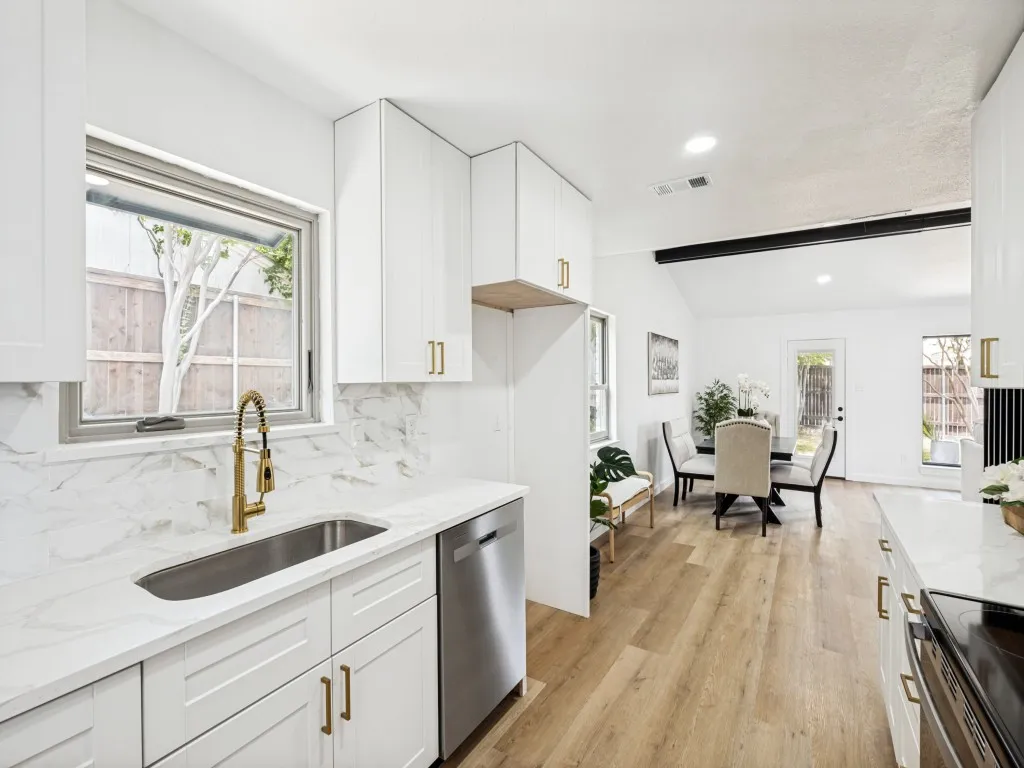 Modern kitchen featuring white cabinetry with brass hardware, a stainless steel sink with gold-finish faucet, and a sleek stainless steel dishwasher