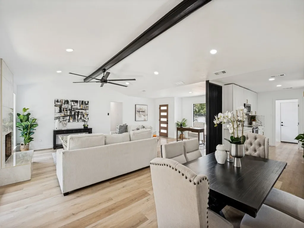 Vaulted ceilings with exposed beam, recessed lighting, wood-finish flooring, fireplace with stone surround, and a modern ceiling fan