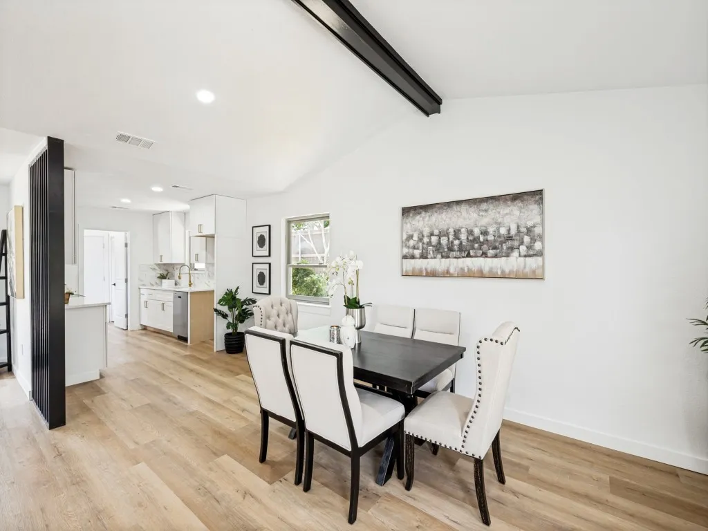 Vaulted ceiling with an exposed beam, wood-finish flooring, recessed lighting, and a kitchen with white cabinetry and a window
