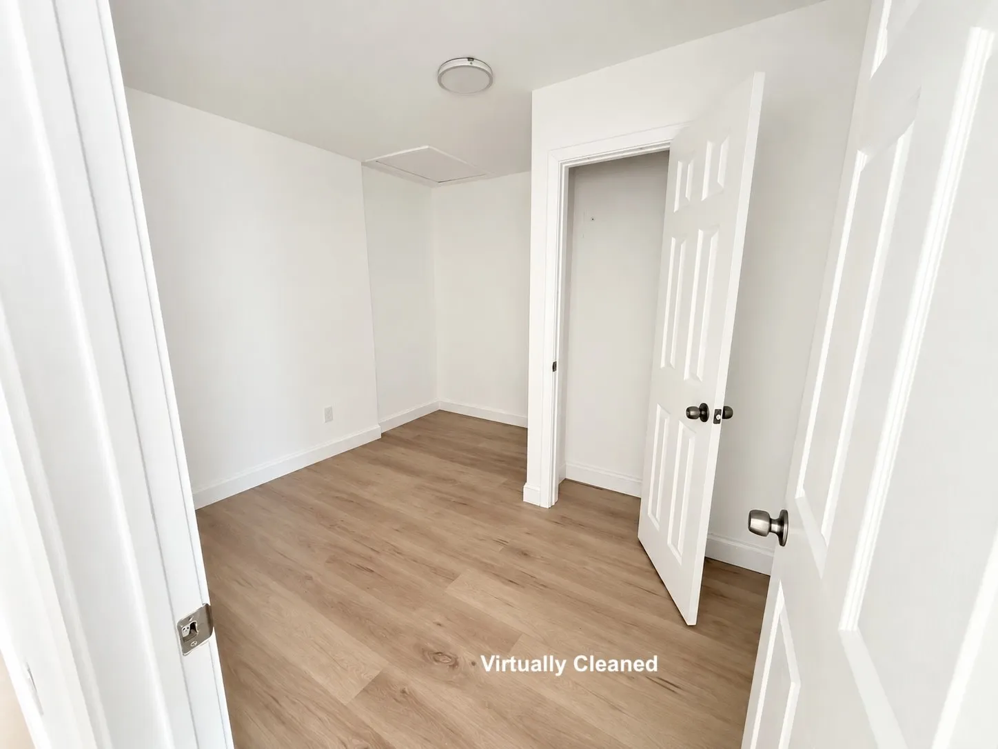 Wood-finish flooring, white paneled door, white walls, and a ceiling-mounted light fixture