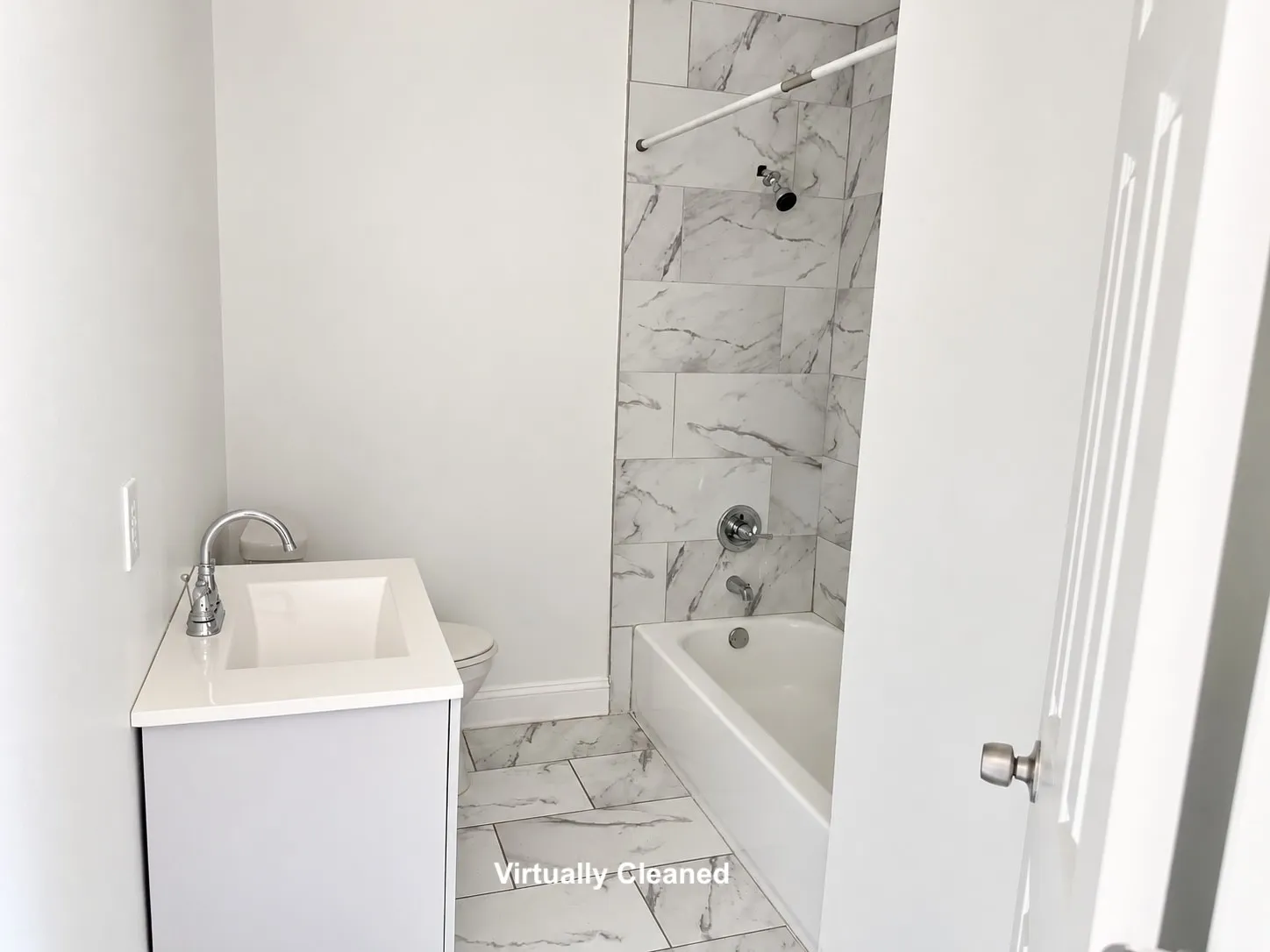 White subway tile shower surround with chrome fixtures, white bathtub, vanity with integrated sink, and tile flooring