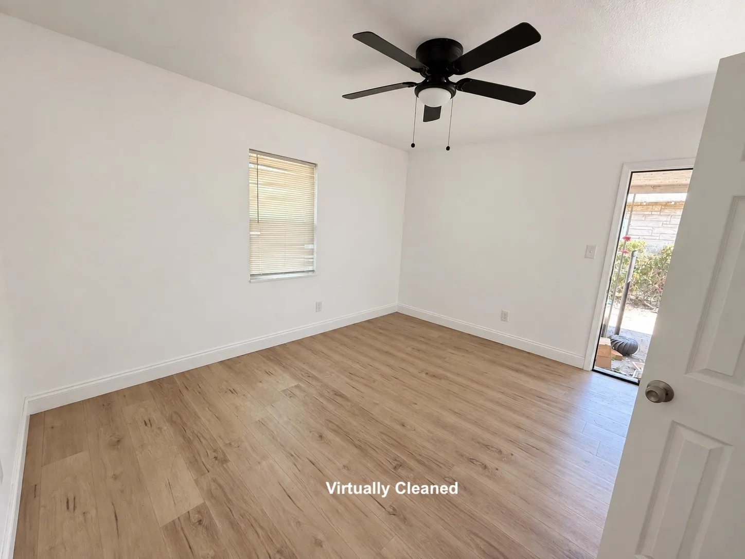 Spacious room featuring wood-finish flooring, a window with horizontal blinds, a ceiling fan with integrated lighting, and a white paneled door