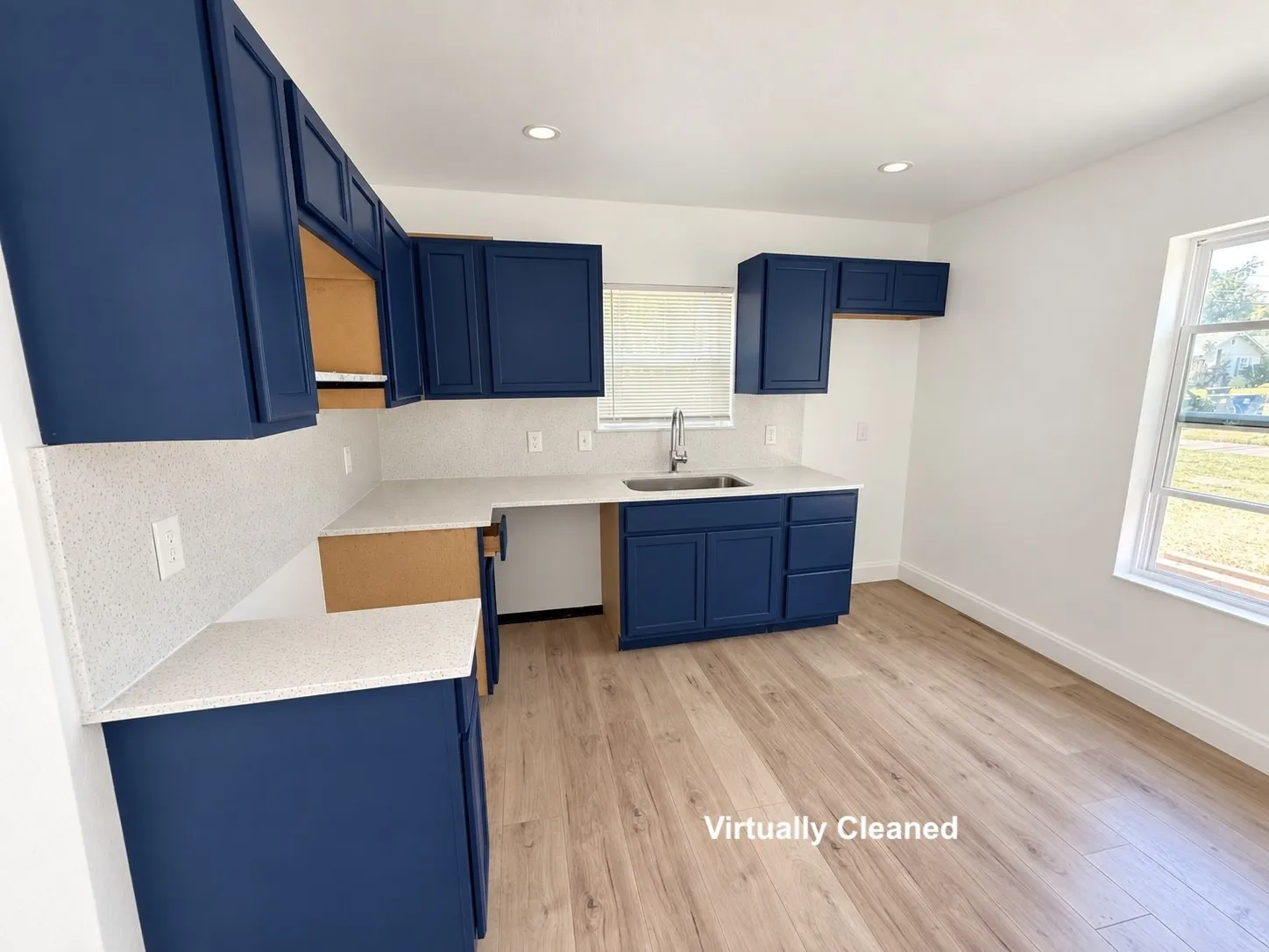 Spacious kitchen featuring deep blue cabinetry, light-toned countertops with matching backsplash, a stainless steel sink with a gooseneck faucet, and wood-finish flooring