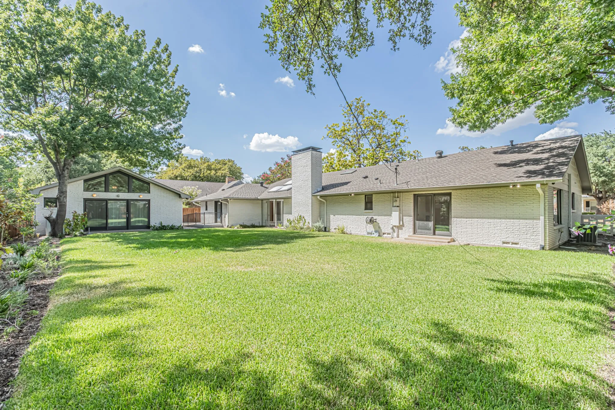 Expansive green lawn with mature trees and a white brick exterior