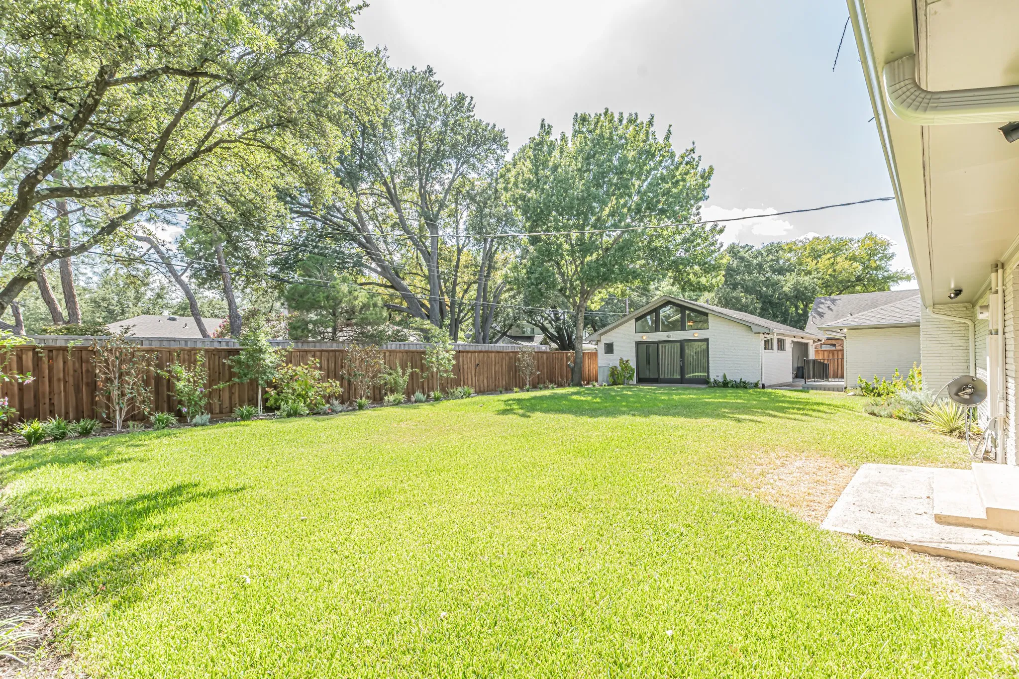 Expansive grassy yard with mature perimeter trees, wood privacy fencing, and a separate structure featuring a pitched roof and large glass panels
