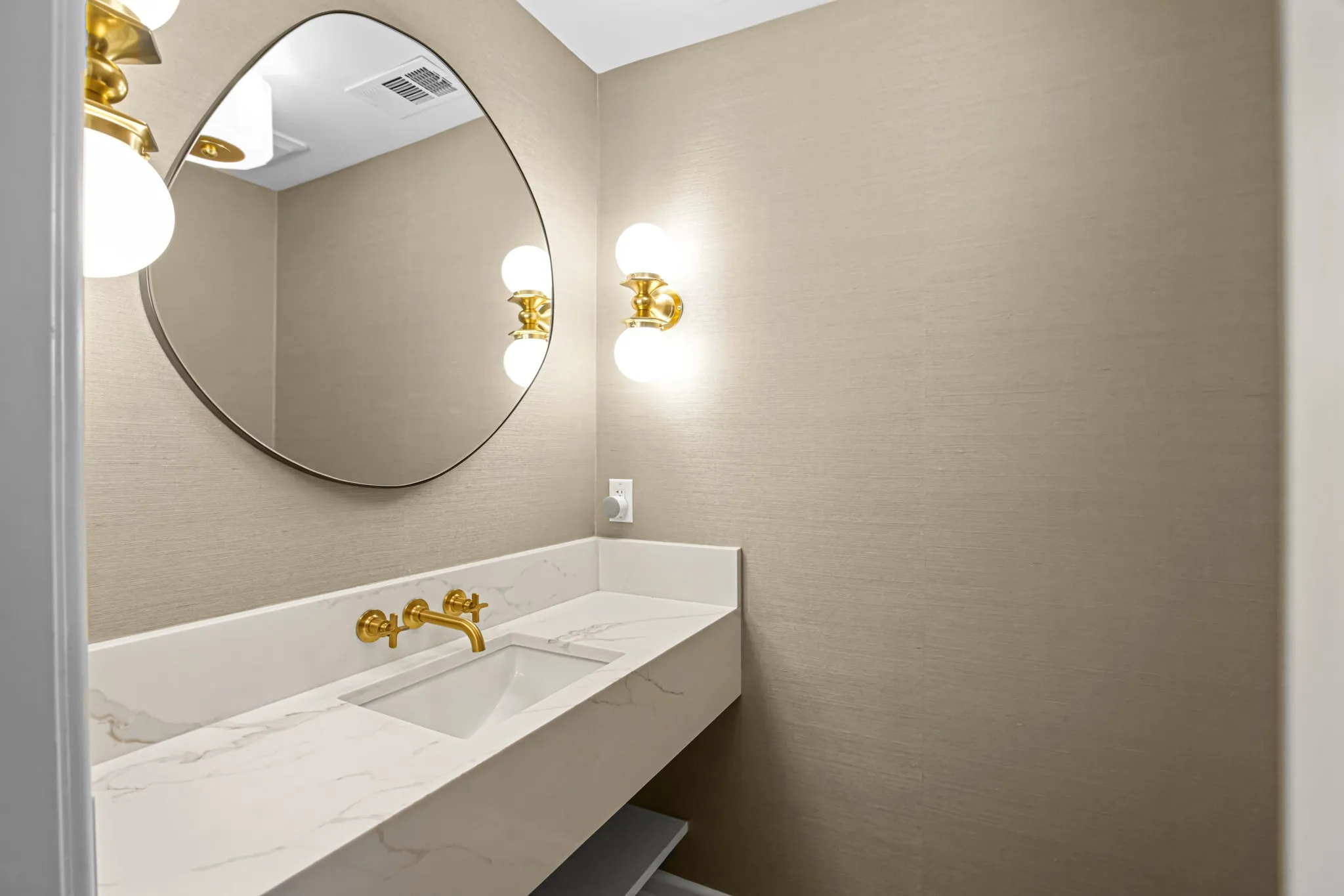 Powder Room features designer touches including grass cloth wallpaper, floating vanity with quartz counters, integrated rectangular sink, gold-tone wall-mounted faucet and light fixtures.