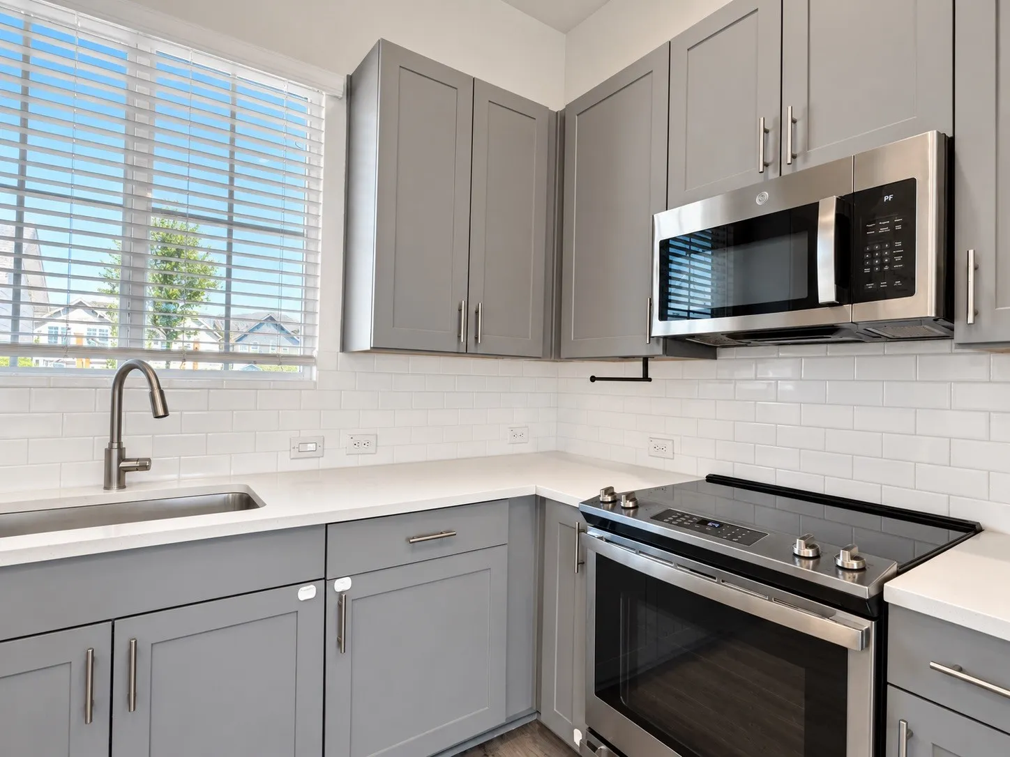 Gray cabinetry with brushed nickel hardware, stainless steel appliances, white subway tile backsplash, light-toned countertops, and a stainless steel sink with a gooseneck faucet