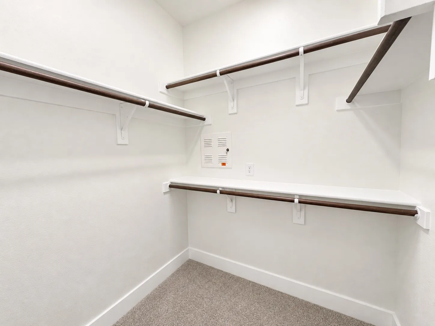 Spacious closet with multiple shelving units, dark wood-finish hanging rods, and light-toned carpeting