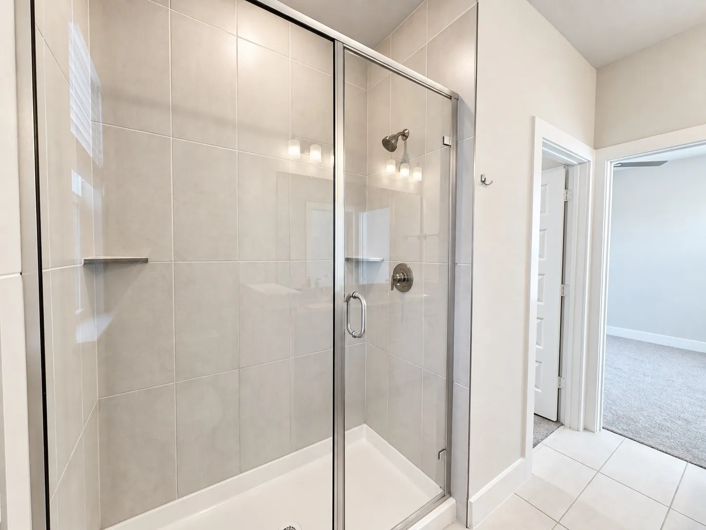 Frameless glass shower enclosure with a rainfall showerhead, integrated shelf, and tiled surround