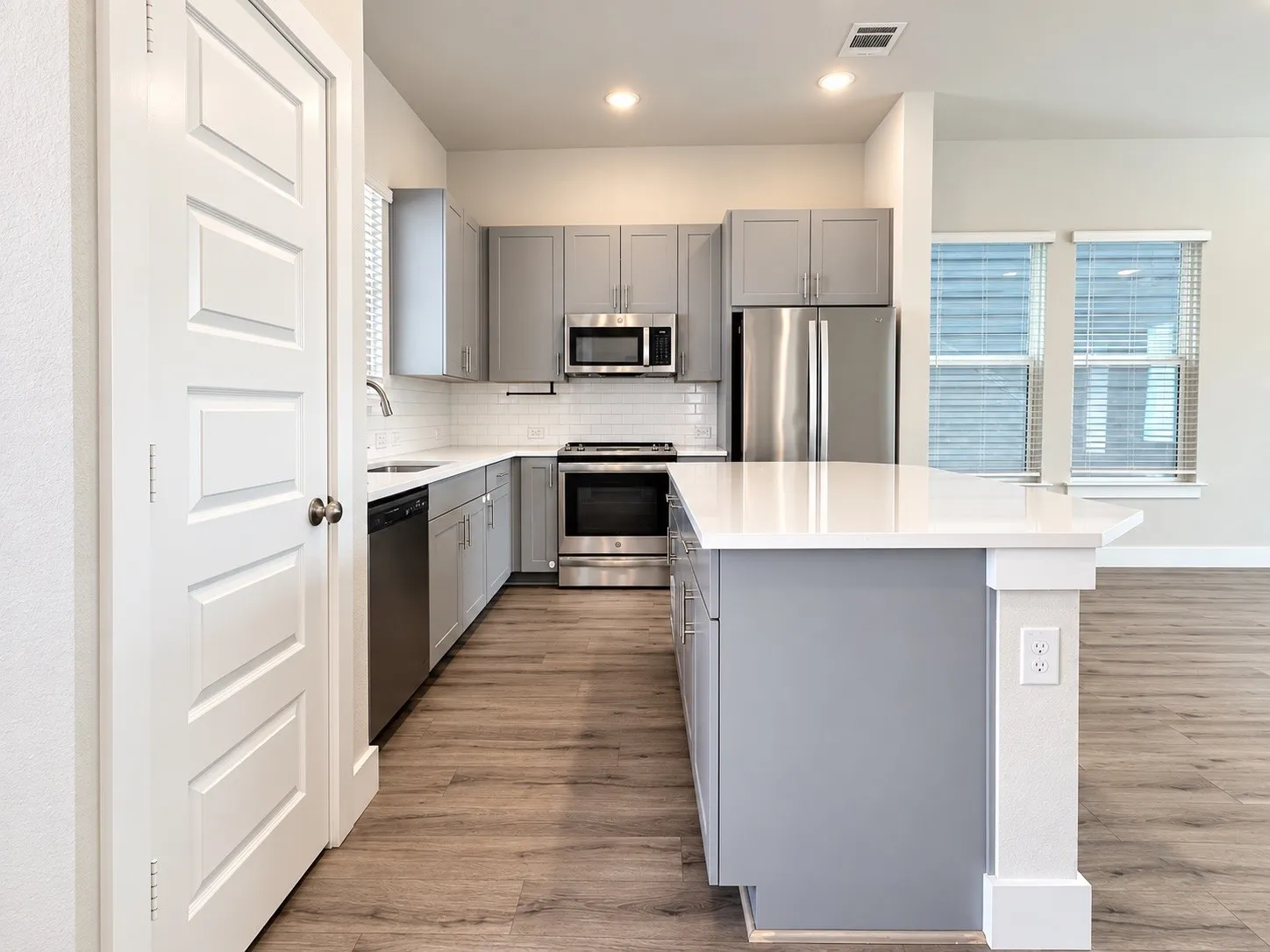 Modern kitchen featuring gray cabinetry, stainless steel appliances, white subway tile backsplash, white countertops, and wood-finish flooring