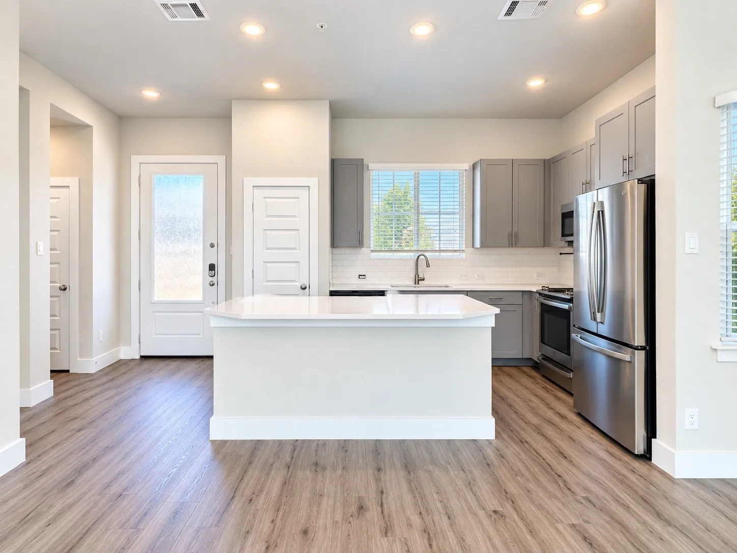 Kitchen featuring wood-finish flooring, a central island with a white countertop, gray cabinetry, stainless steel appliances, and a white subway tile backsplash