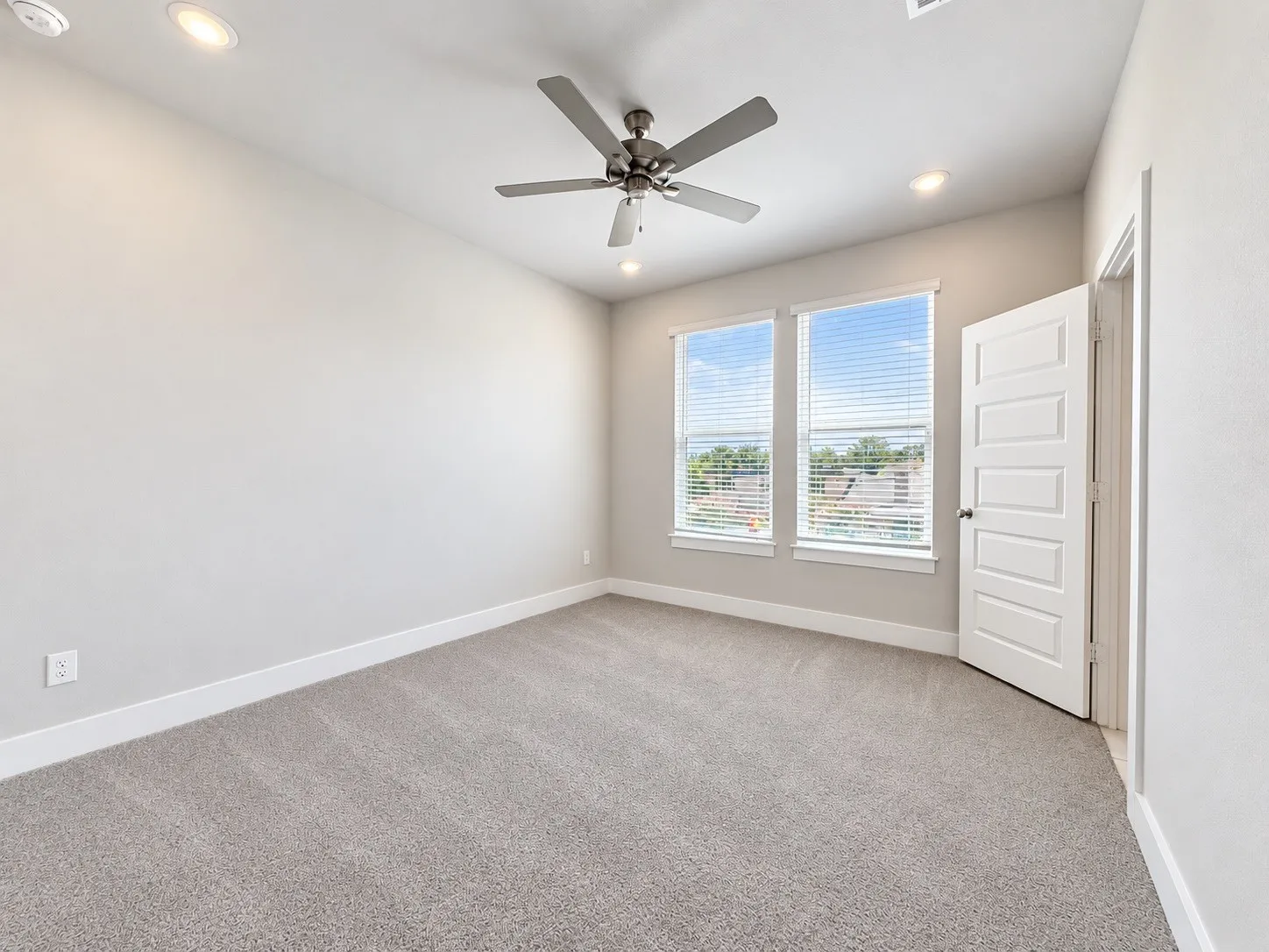 Spacious room featuring neutral carpeting, recessed lighting, a ceiling fan, and two windows with blinds