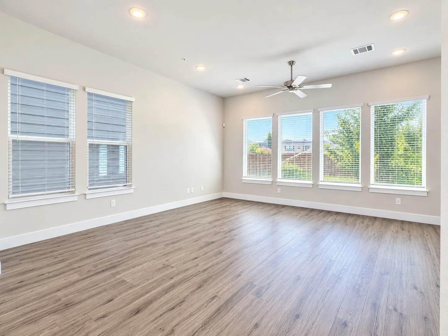 Spacious room featuring wood-finish flooring, recessed lighting, and multiple windows with blinds