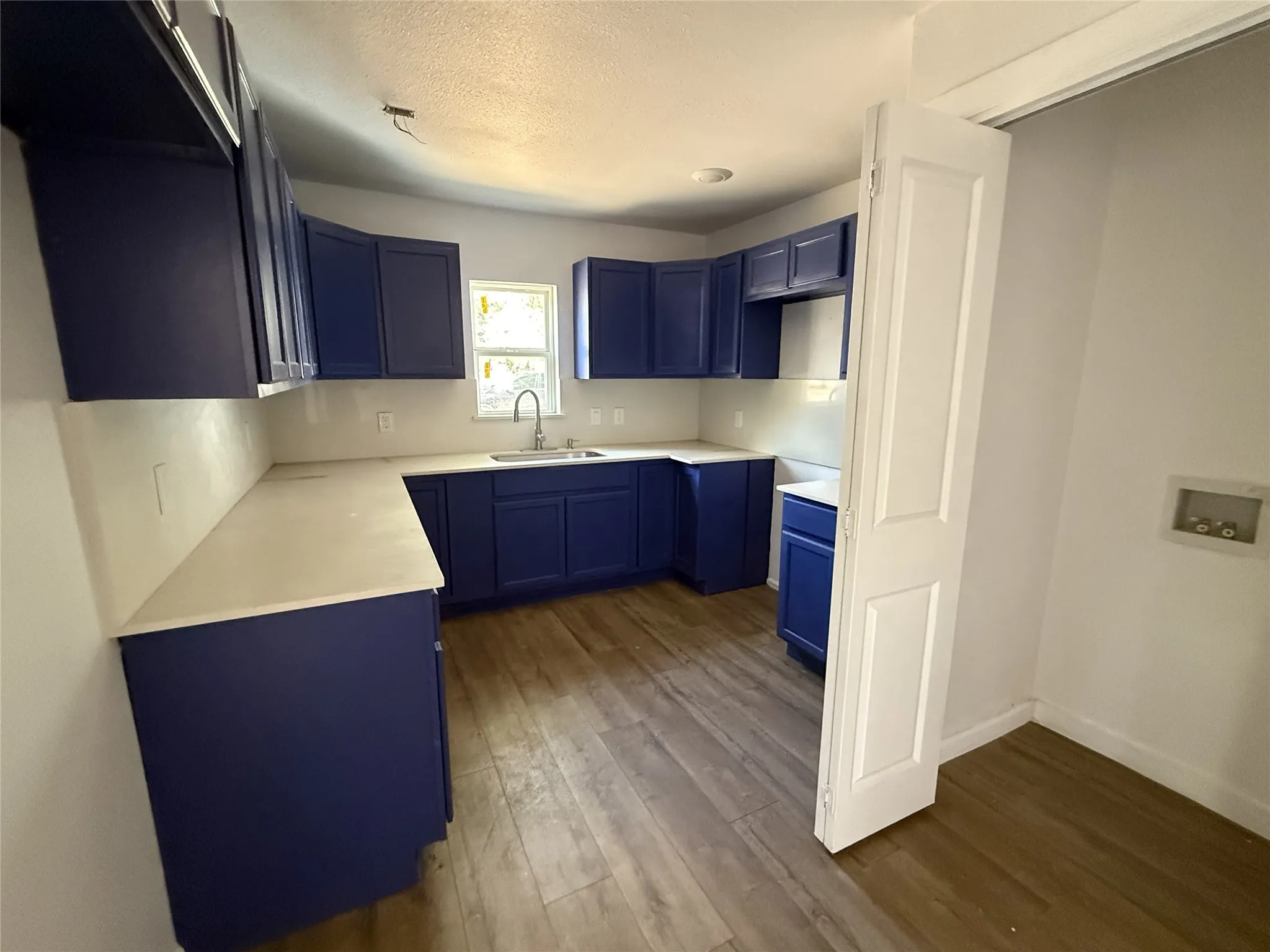 Newly installed blue cabinetry, extensive light-toned countertops, wood-finish flooring, a stainless steel sink, and a utility hookup