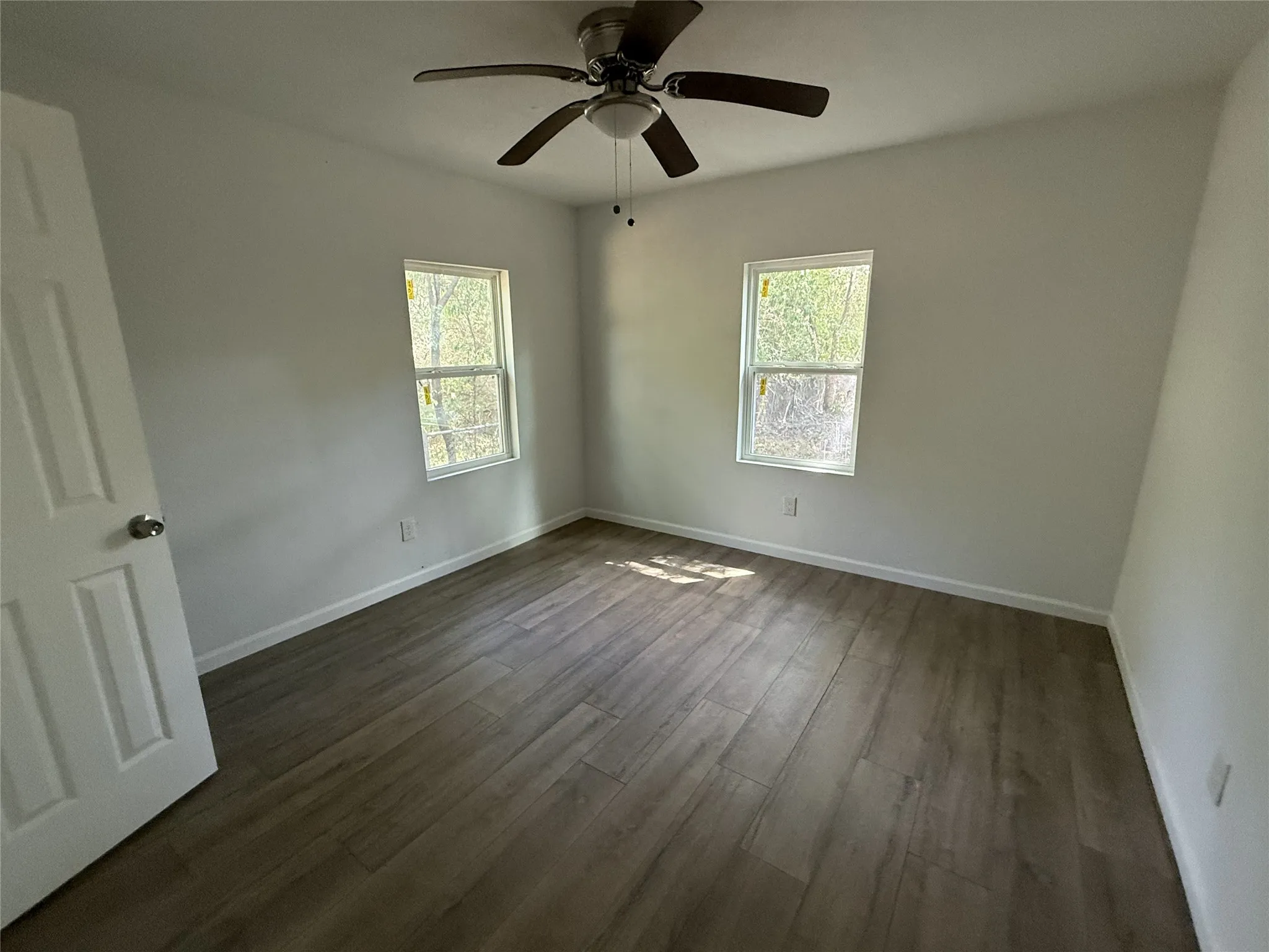 Recessed ceiling fan with integrated lighting, two windows with white trim, wood-finish flooring, and white baseboards