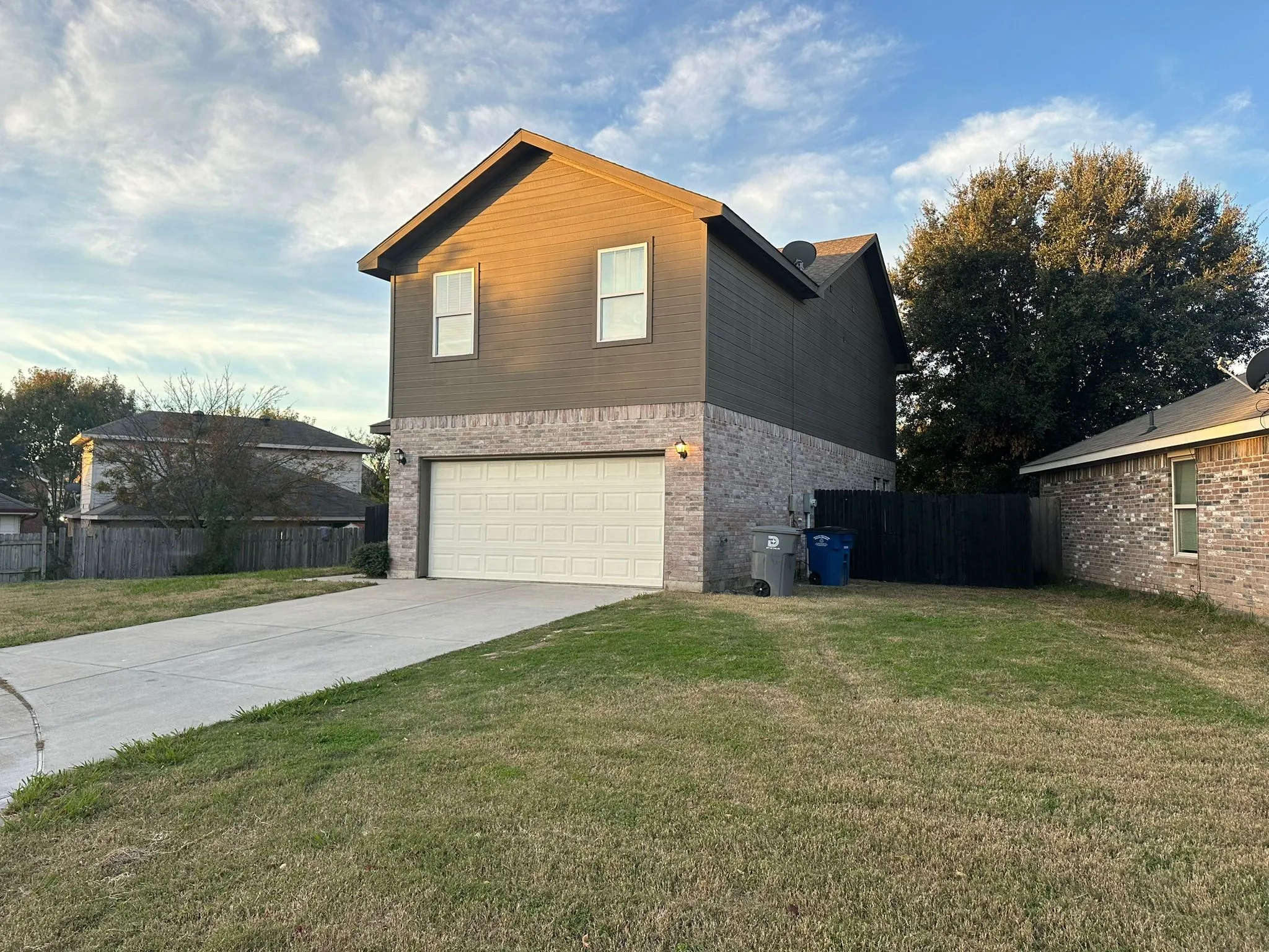 Exterior featuring brick and horizontal siding, an attached garage, a concrete driveway, and a fenced side yard