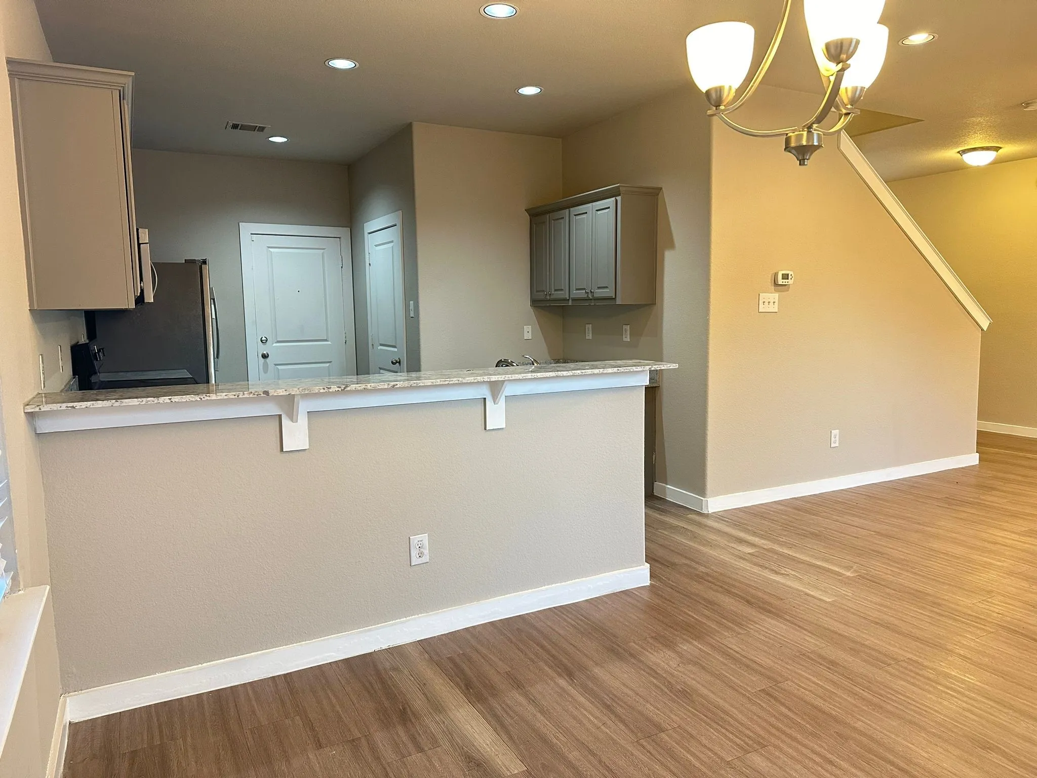 Wood-finish flooring, recessed lighting, and a chandelier illuminate the open-concept living space