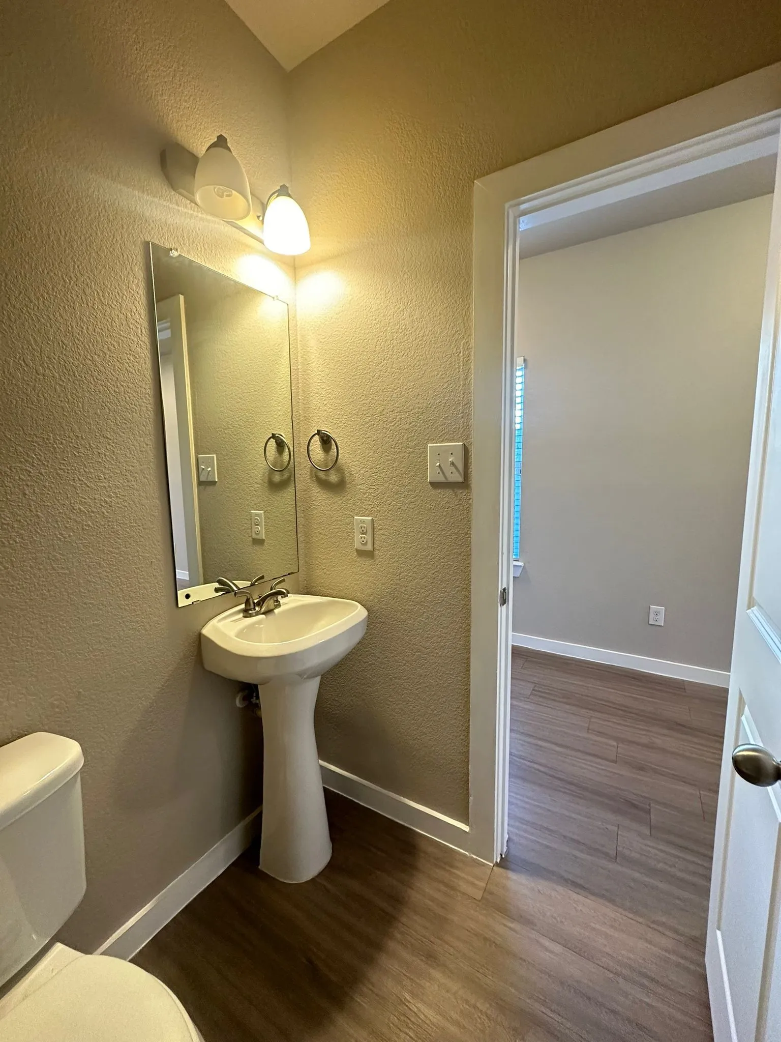 Pedestal sink with chrome fixtures, wall-mounted mirror, and wood-finish flooring