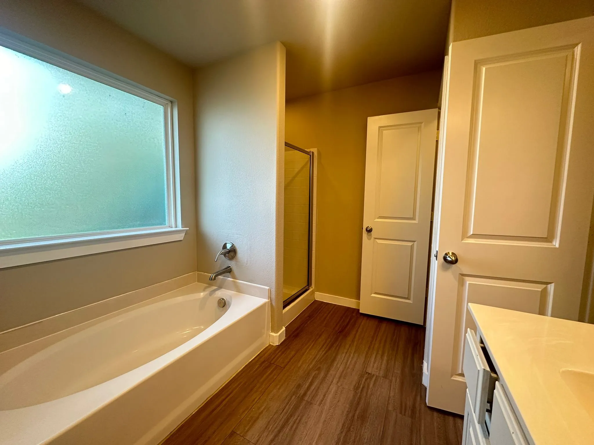 Bathroom featuring a bathtub, separate shower with glass enclosure, wood-finish flooring, a vanity with an integrated sink, and a privacy window