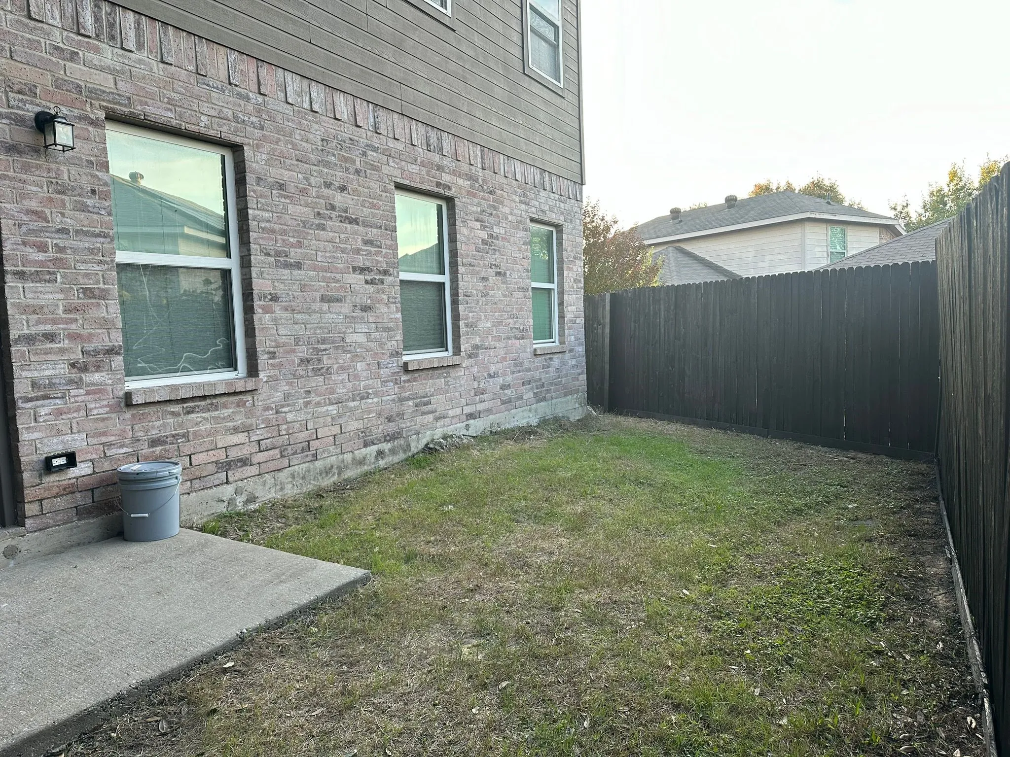 Brick and siding exterior with multiple windows, concrete patio, and a wood privacy fence