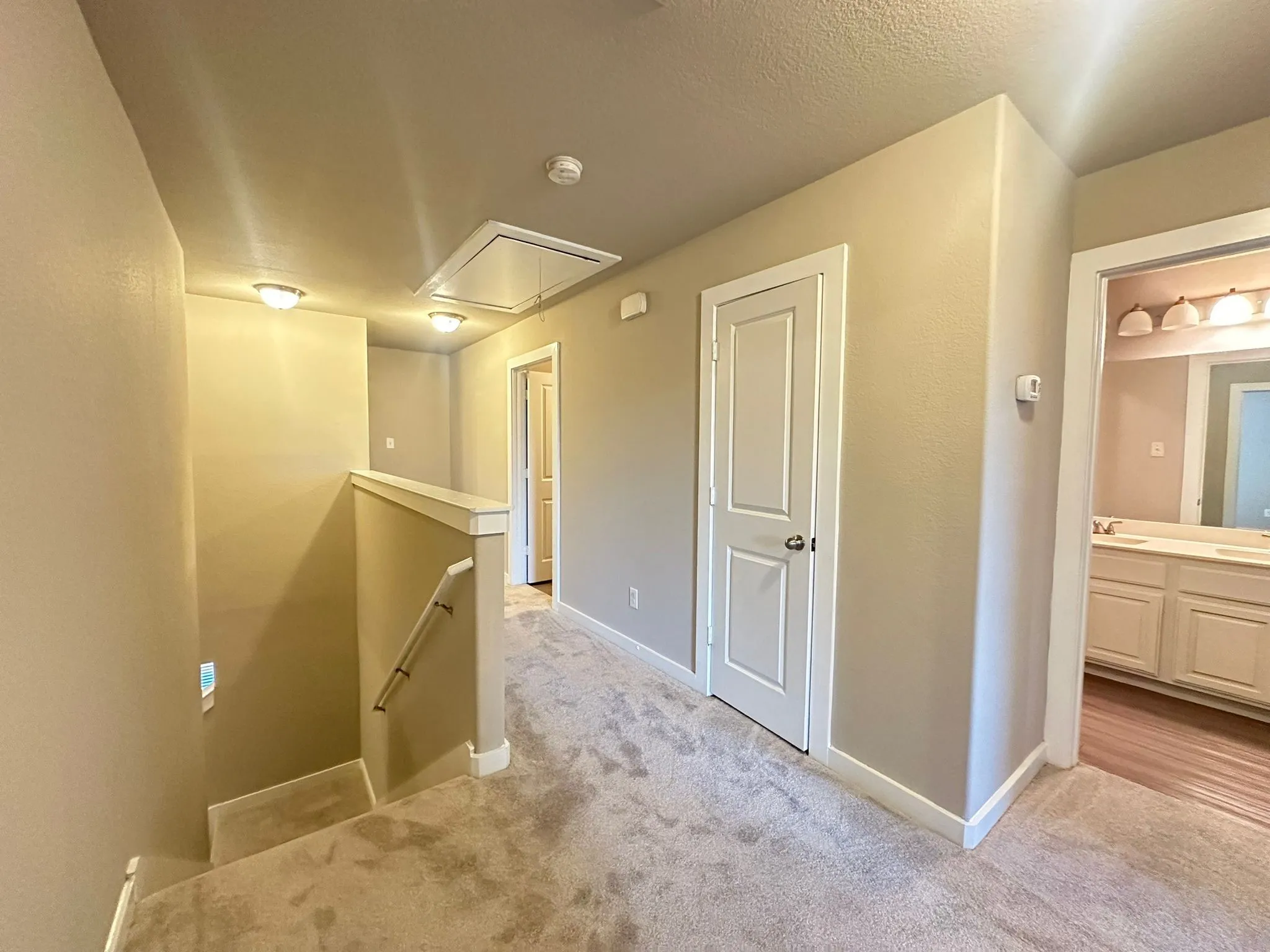 Carpeted hallway with flush-mount lighting, white paneled doors, and a staircase with a white handrail