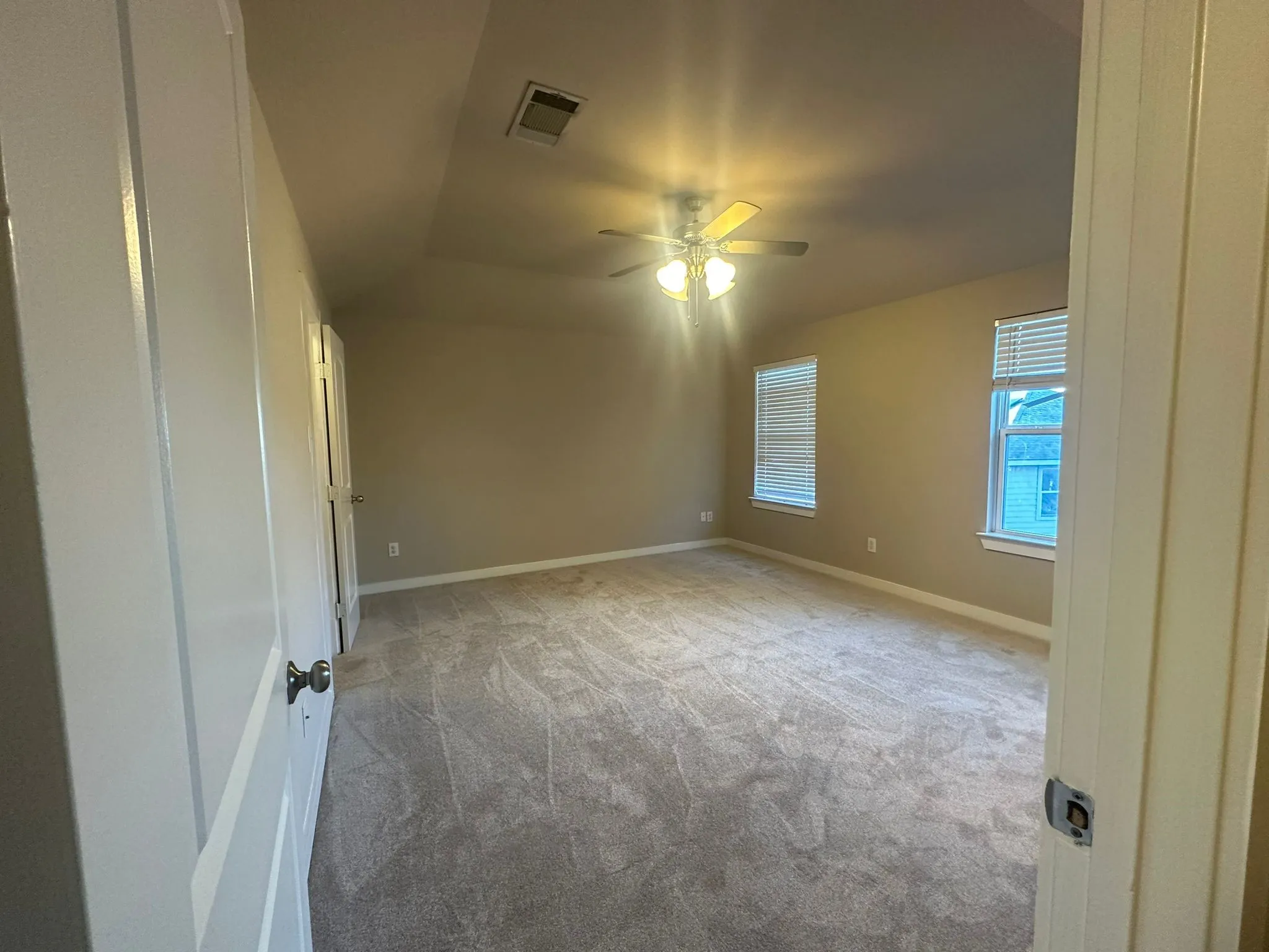 Spacious room with plush carpeting, two windows with blinds, a ceiling fan with light, and light neutral wall paint