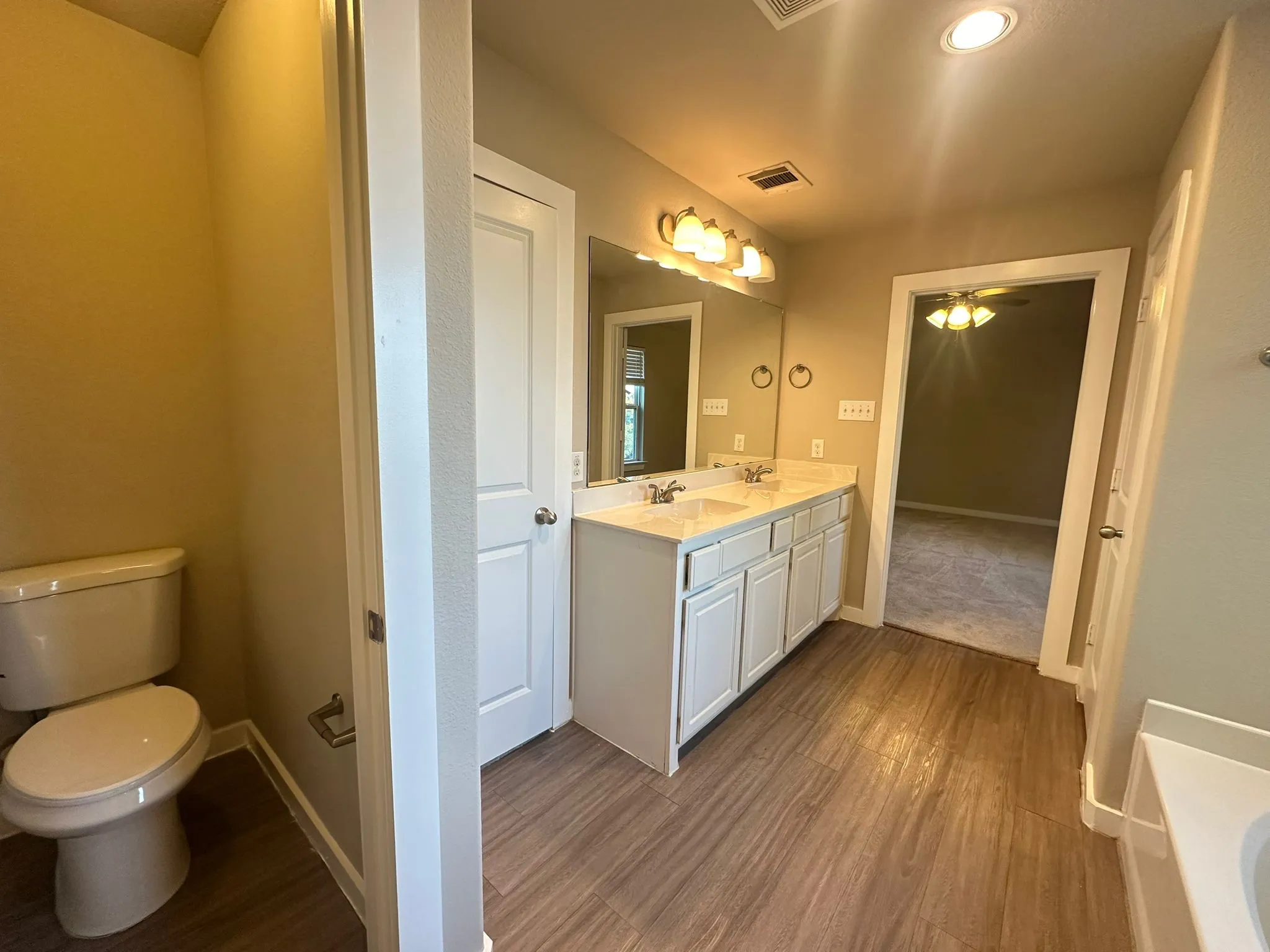 Dual vanity with integrated sinks, wood-finish flooring, white cabinetry, and recessed lighting