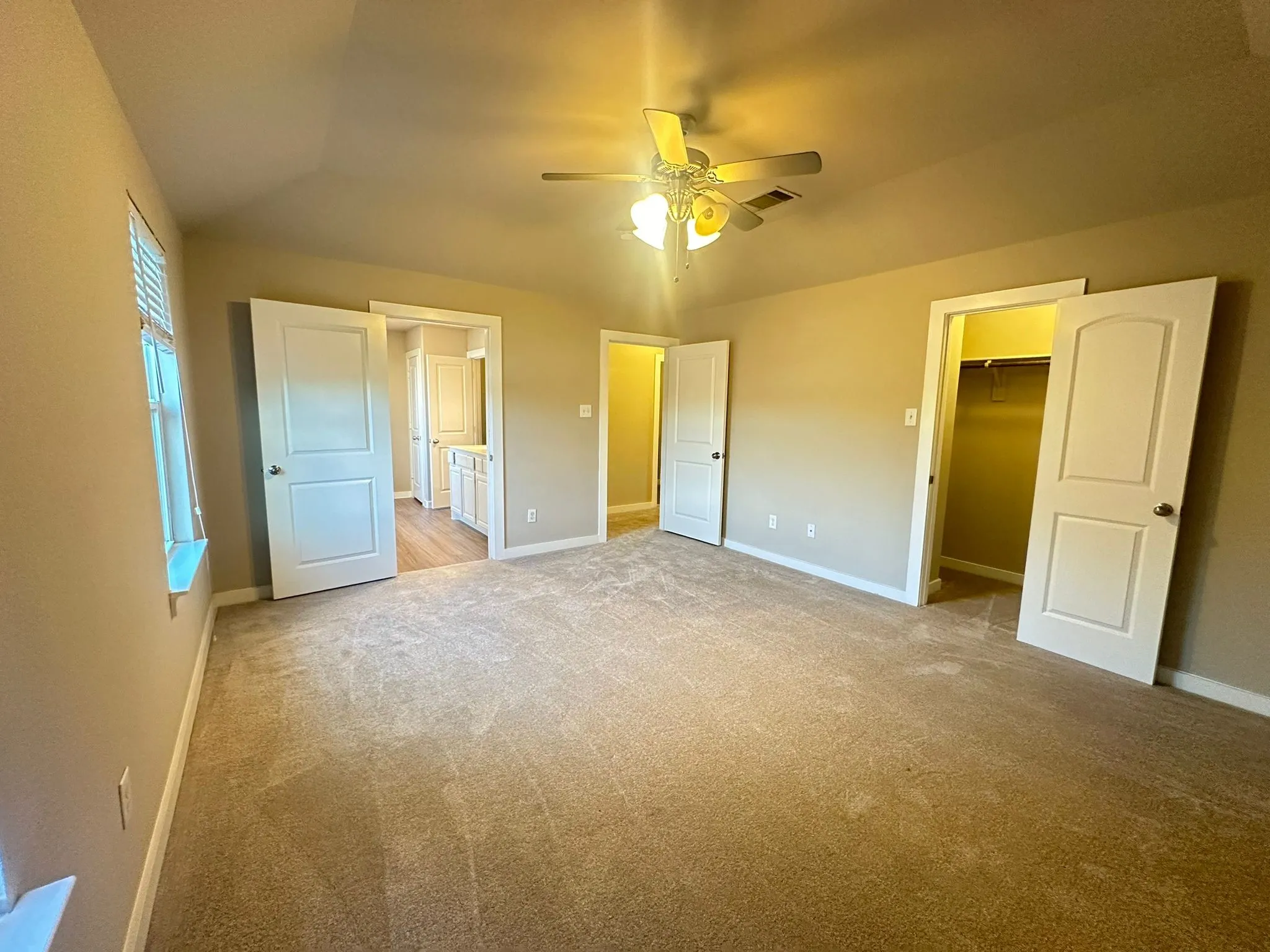 Carpeted room with a vaulted ceiling, ceiling fan, and multiple doorways